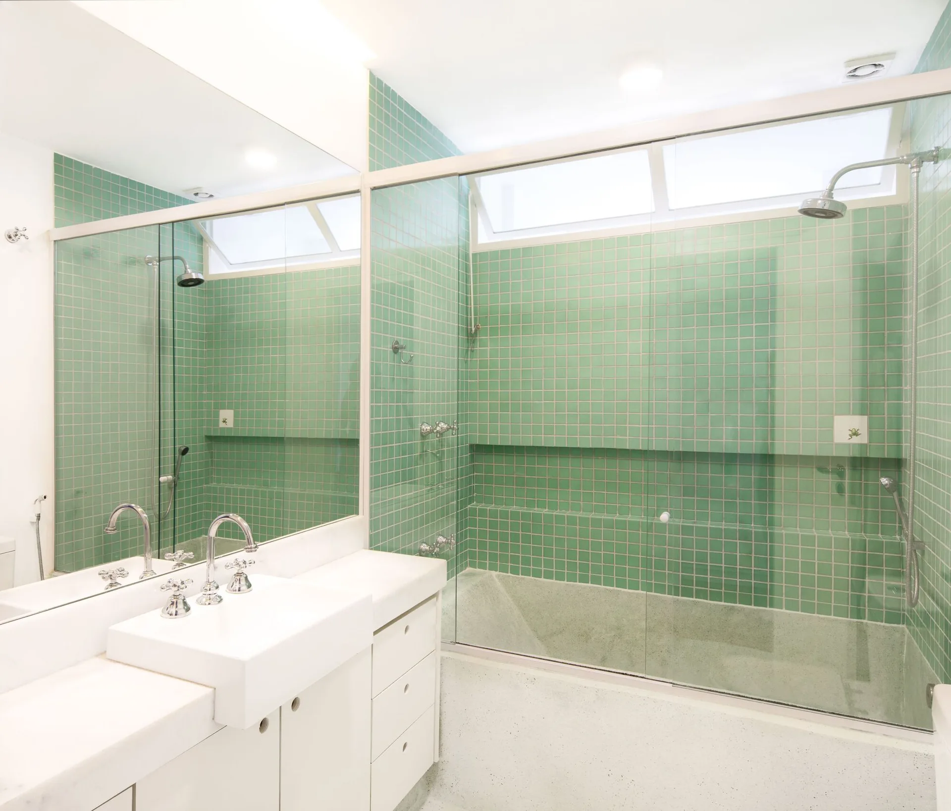 A bright bathroom features walls covered in green grid tiles, a white sink vanity with chrome faucets, and a glass shower enclosure.