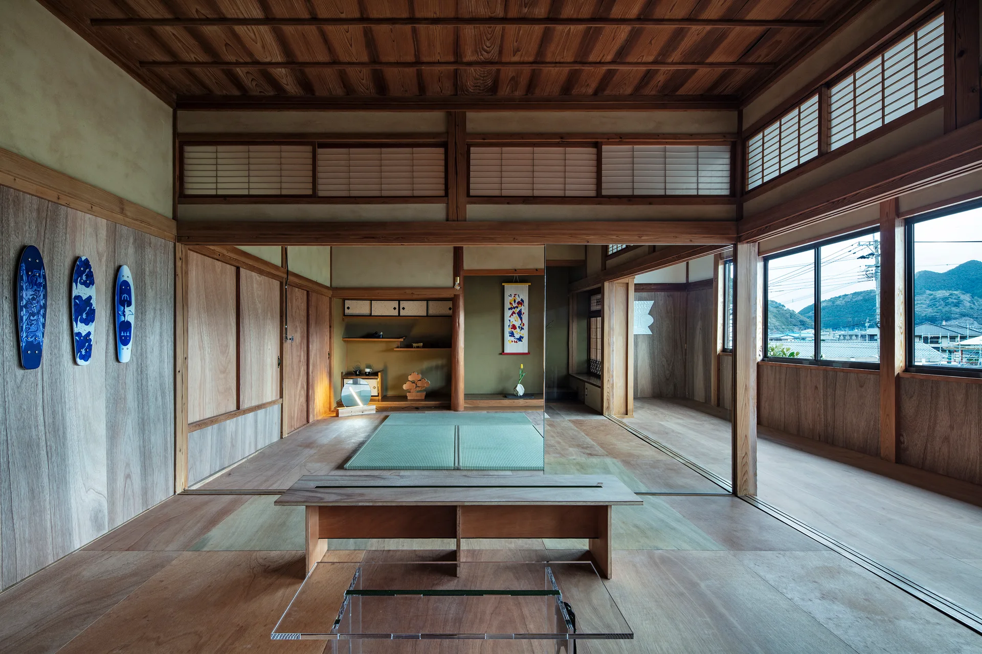 A traditional Japanese room features natural wood paneling, tatami mats, a wooden bench, and three blue decorative surfboards mounted on the wall.