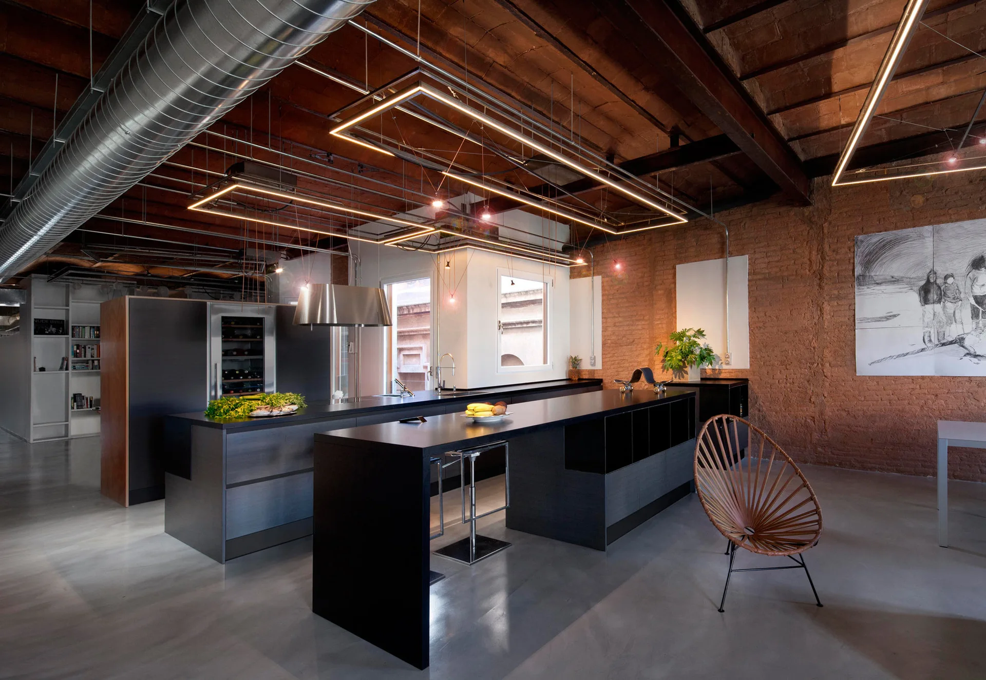 An industrial loft kitchen features a matte black island, exposed brick walls, and rectangular linear pendant lights suspended from a beamed ceiling.