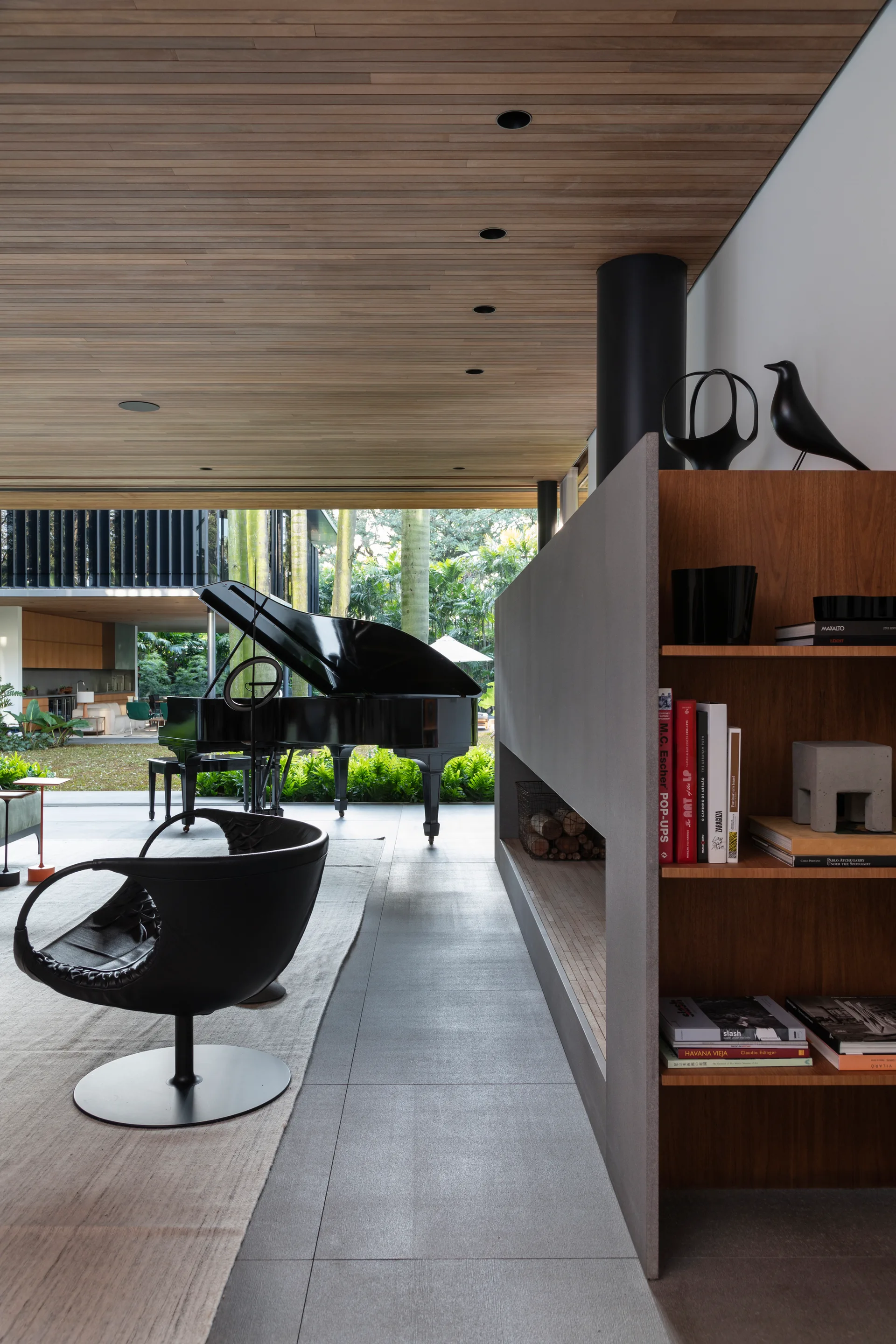 A modern living room features a wood plank ceiling, a grey fireplace room divider with wooden shelves, a black swivel chair, and a grand piano.