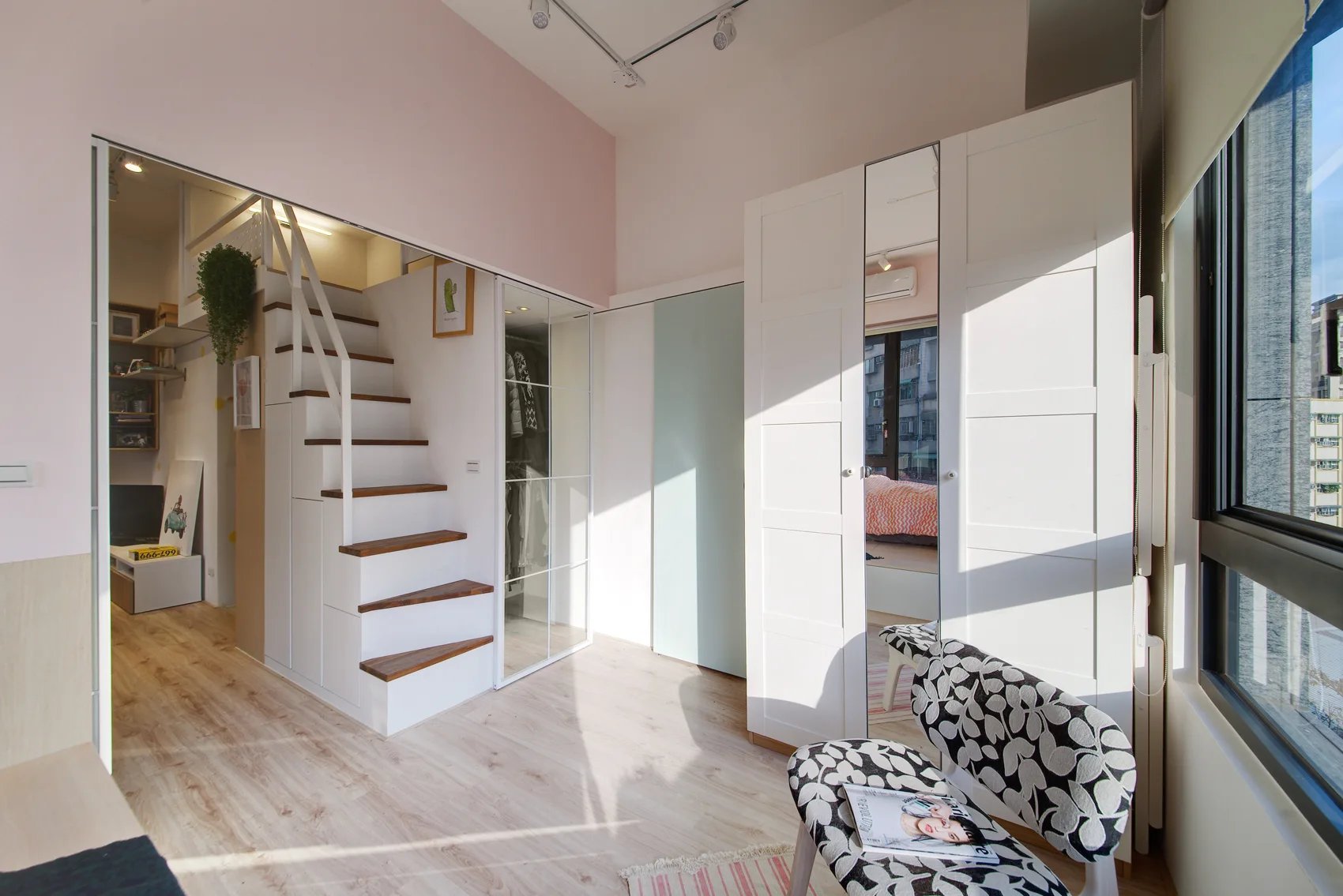 A minimalist loft bedroom featuring a white staircase with wood treads, integrated storage, and a patterned accent chair.