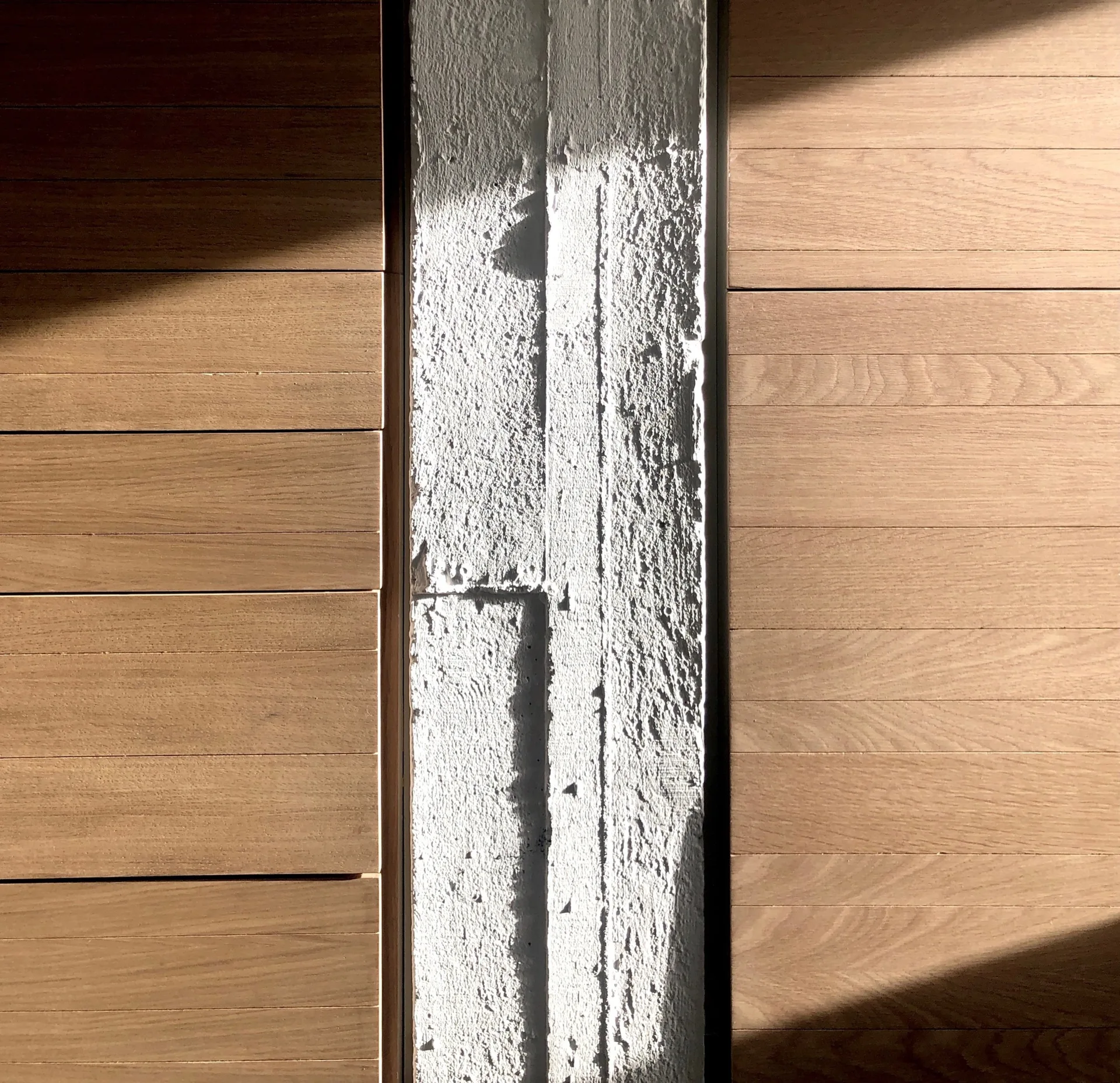 A close-up architectural view of horizontal warm wood planks flanking a vertical, rough-textured grey concrete pillar in strong light.