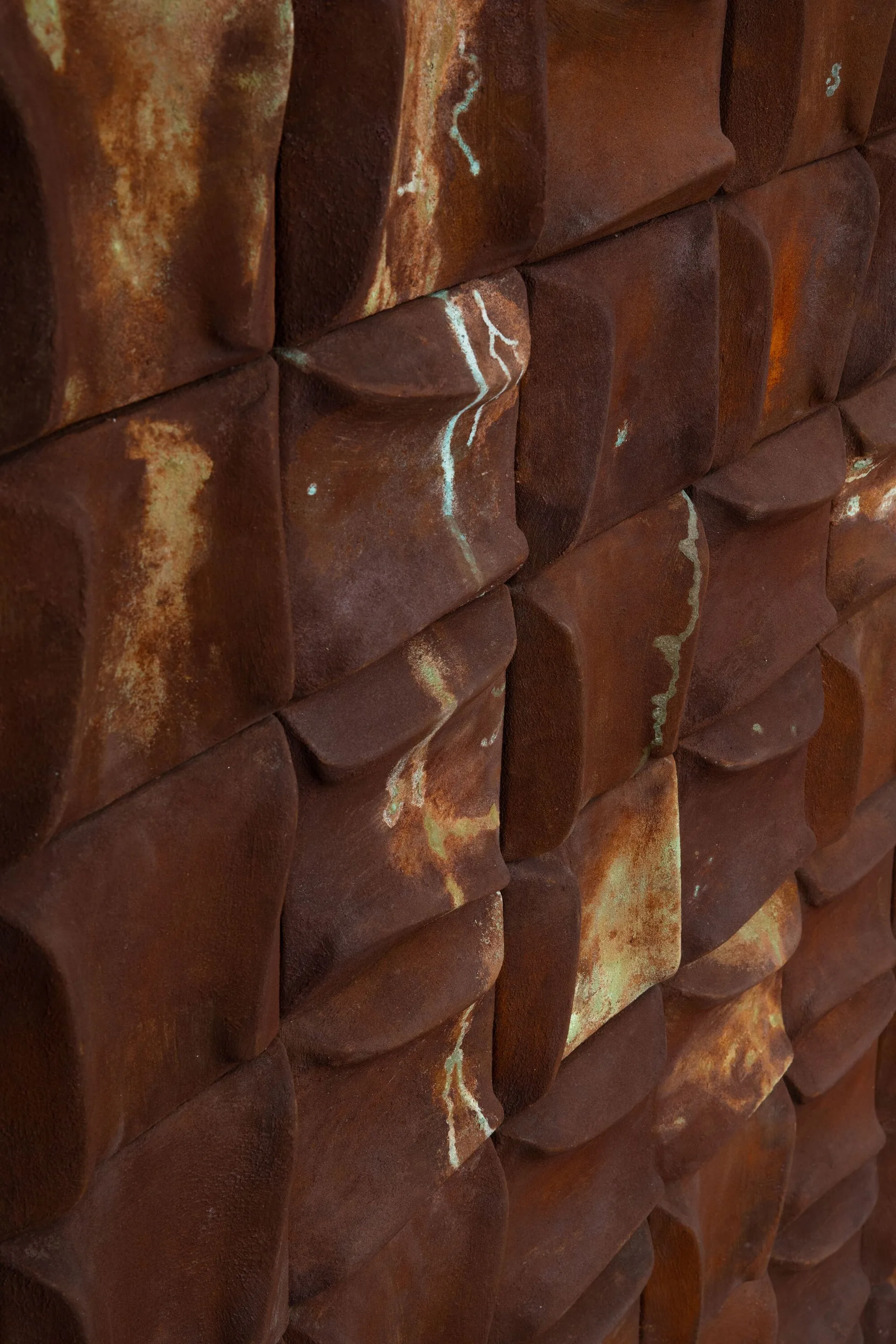 A close-up view of textured geometric wall cladding made of rusted brown metal with subtle streaks of green verdigris patina.