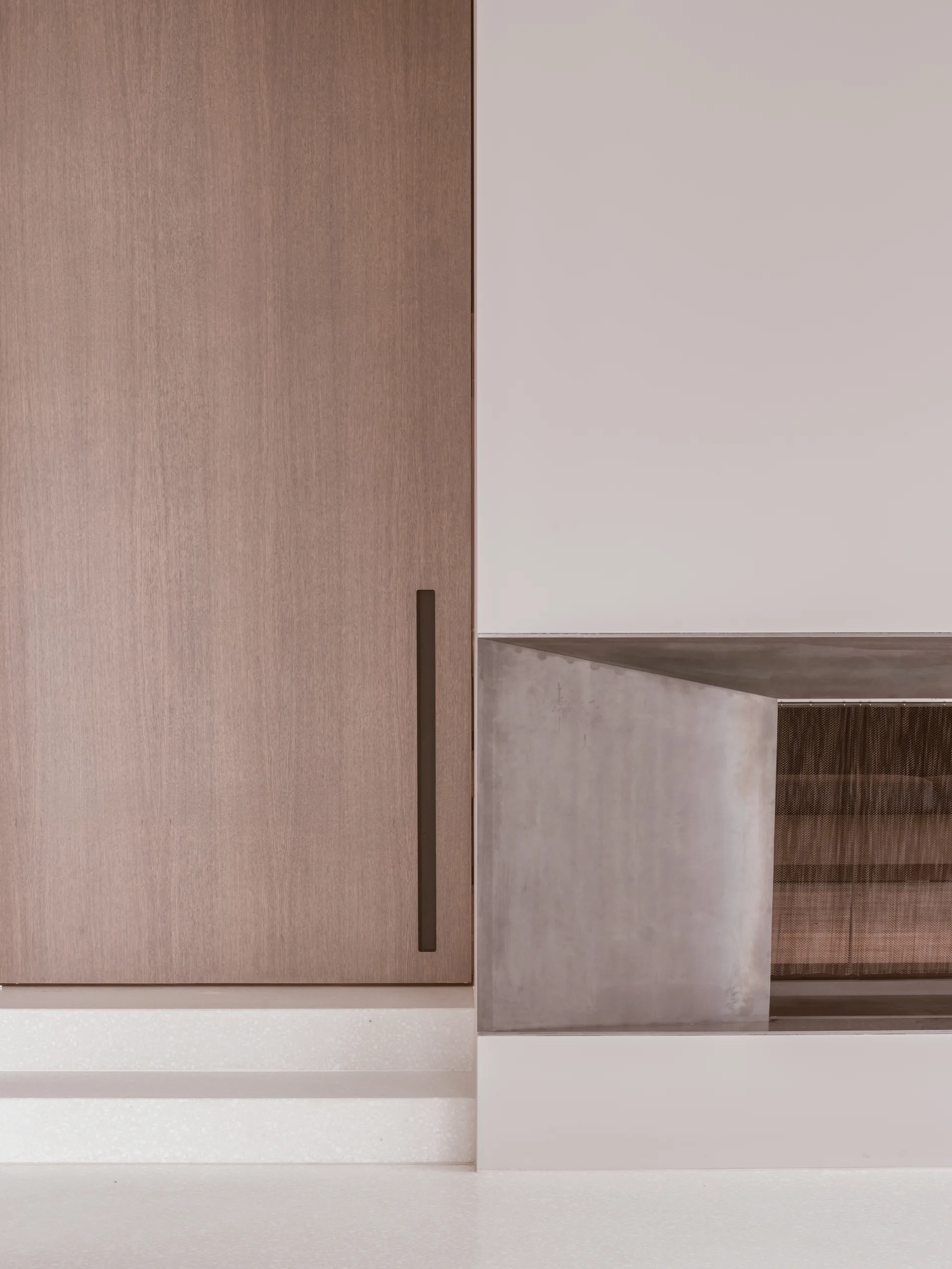 A minimalist architectural detail showing a wooden panel door with a recessed black handle next to an integrated metal fireplace and light terrazzo steps.