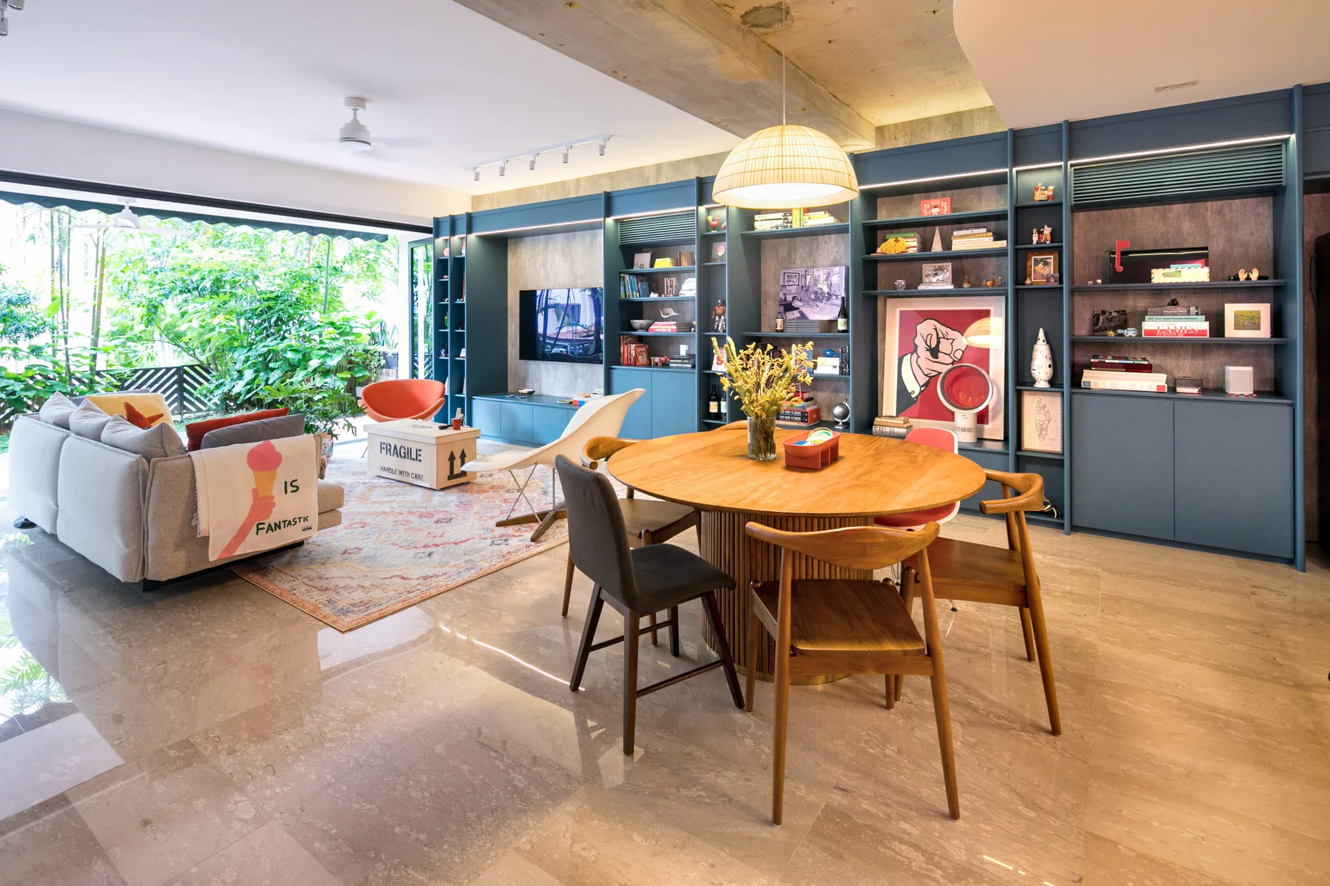 A spacious open-plan living and dining room featuring a large blue built-in shelving unit, a round wooden dining table, and sliding glass balcony doors.