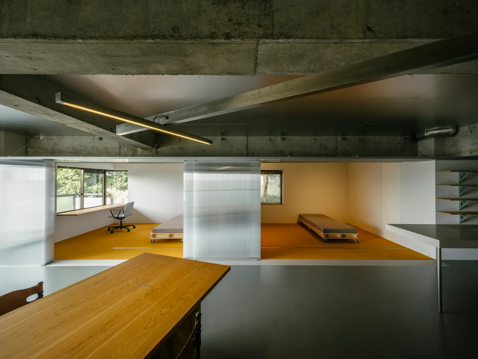 An industrial loft space with an exposed concrete ceiling, yellow flooring, two rolling platform beds, and translucent sliding polycarbonate screens.