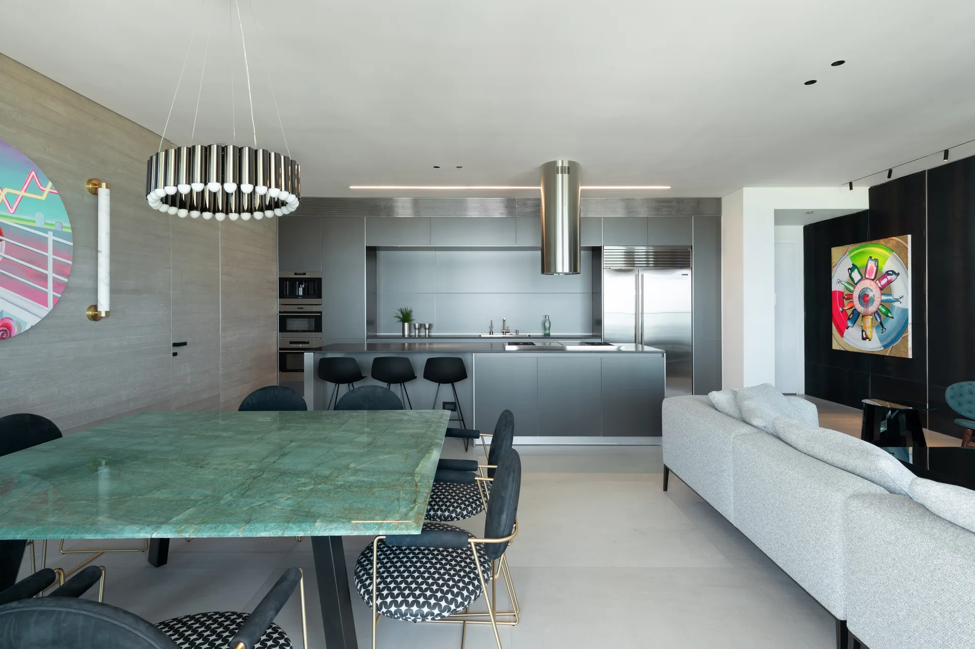An open-concept kitchen features flat-panel grey cabinets, a matching island with bar stools, and a large dining table topped with green marble.
