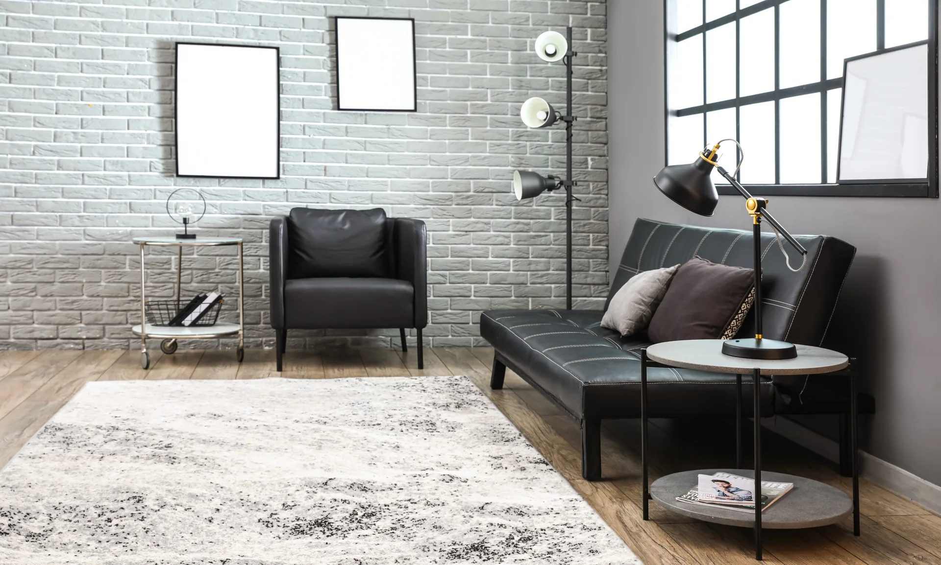 A modern living room features a black leather sofa, a matching armchair, a grey painted brick wall, and a mottled area rug.