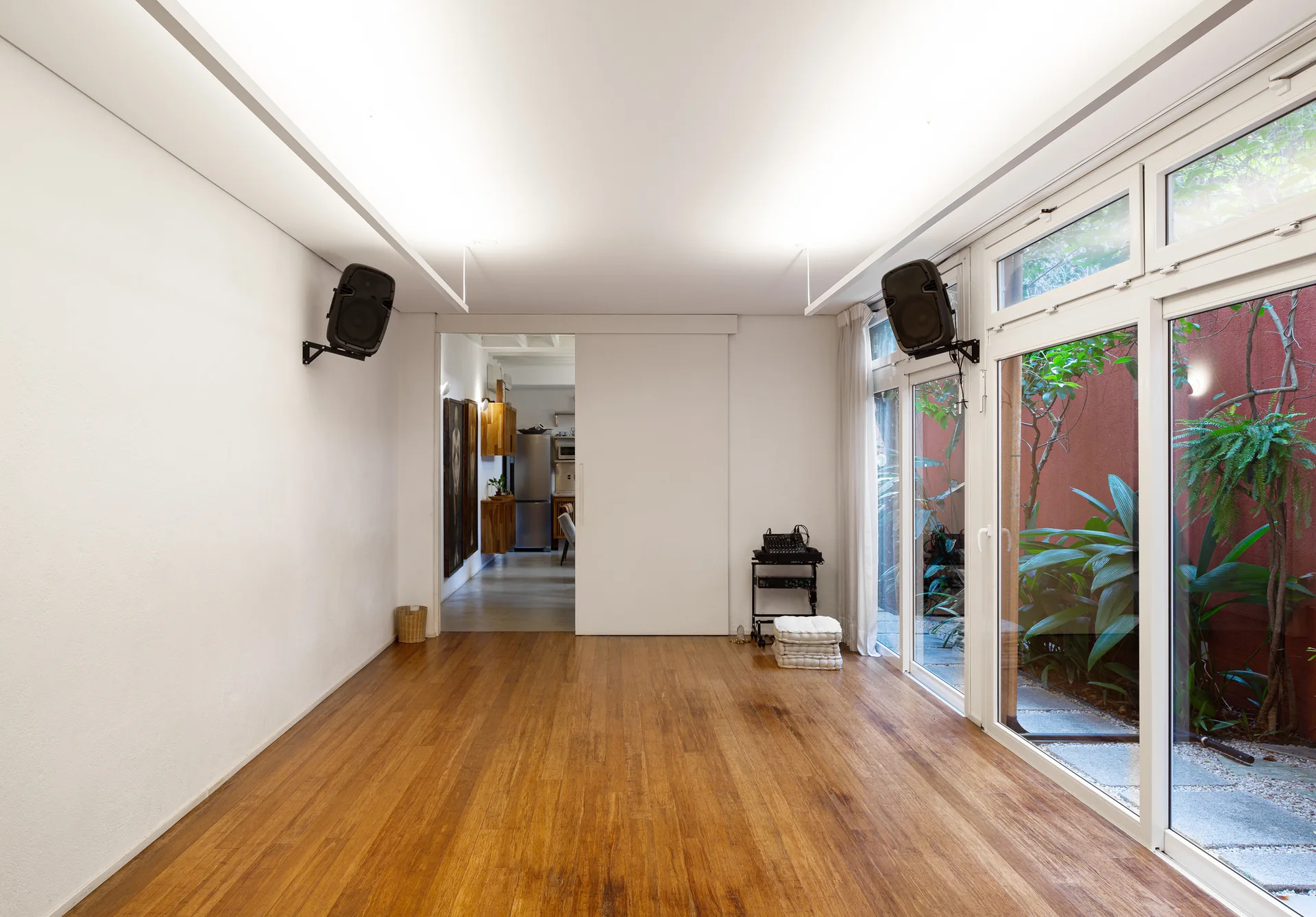 A minimalist room with warm hardwood flooring, clean white walls, and large sliding glass doors leading to a courtyard.