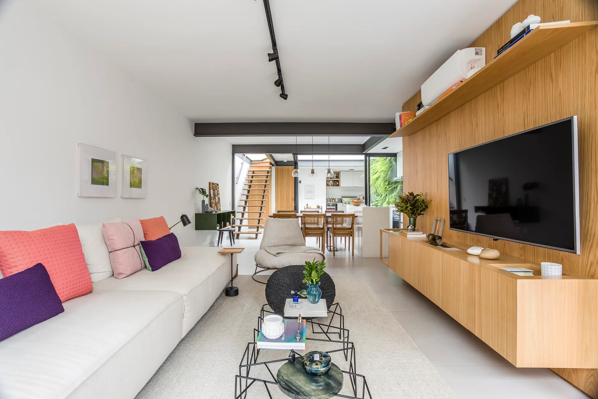 A modern open-plan living room with a white sofa, a long wooden floating media console, and a geometric black metal coffee table.