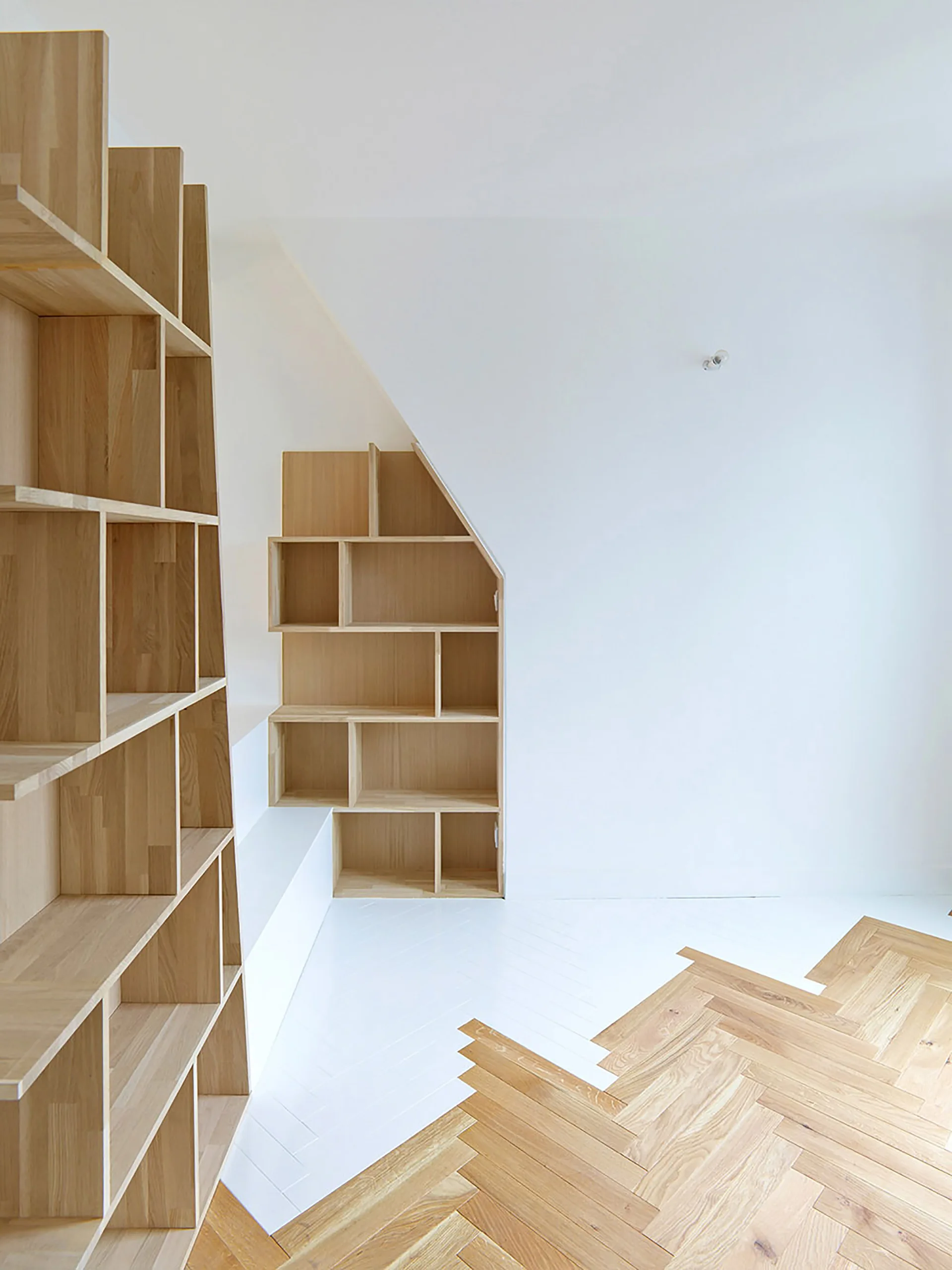 Minimalist light wood built-in shelving unit standing against a white wall next to a white and herringbone wood floor transition.
