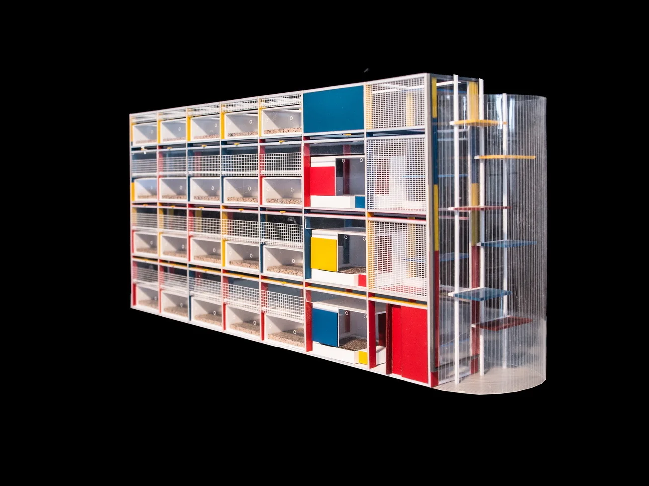 A modernist architectural scale model features a white geometric grid structure with red, blue, and yellow panels on a solid black background.