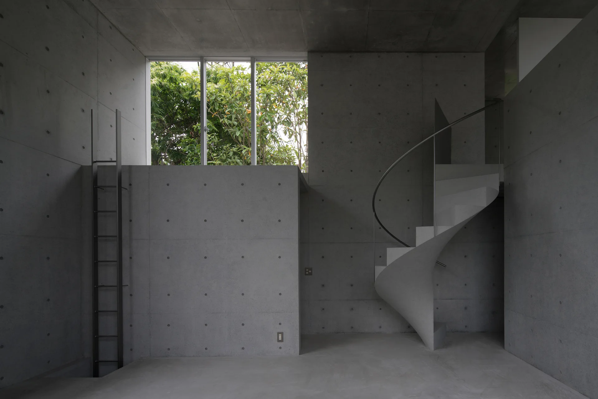 A minimalist raw concrete room features a central concrete spiral staircase, a black metal ladder, and a high window framing green trees.