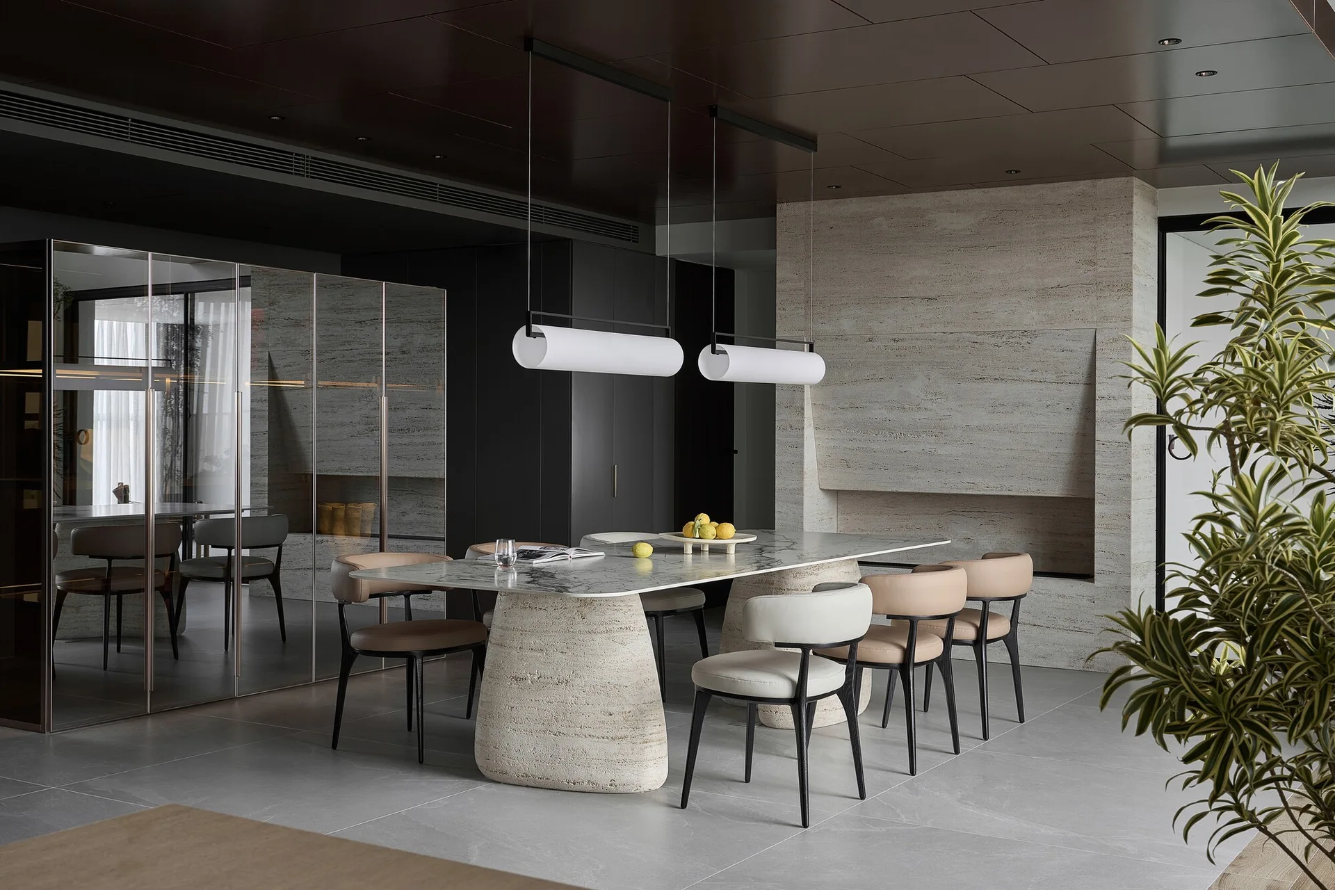A modern dining room featuring a marble table with thick stone pedestal bases, beige and grey leather chairs, and two cylindrical hanging pendant lights.