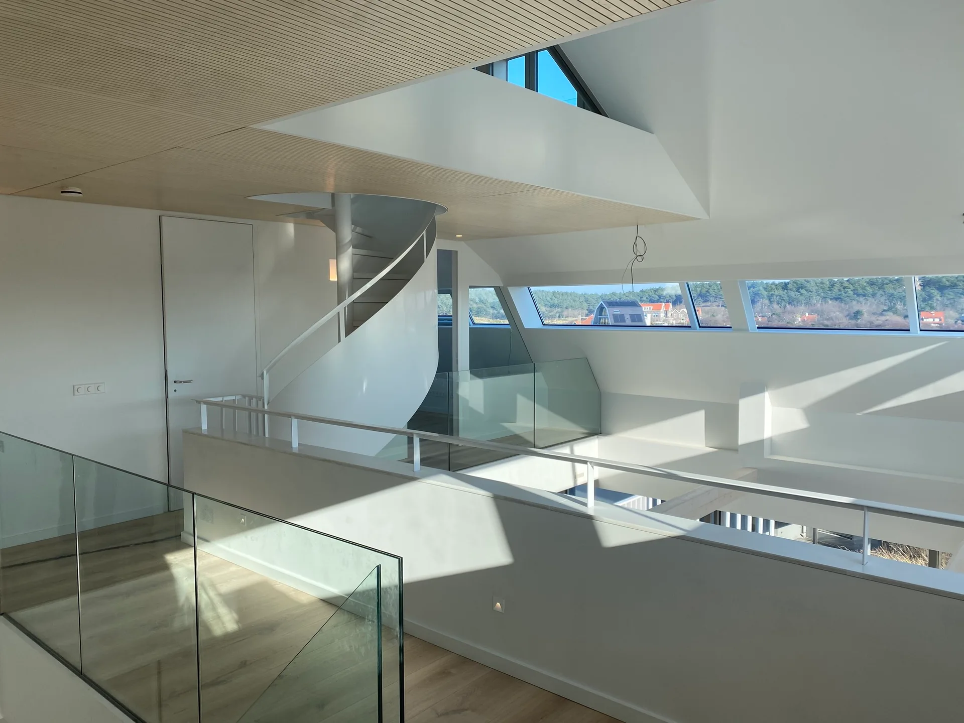 A minimalist mezzanine features a white spiral staircase, glass railings, a slatted wood ceiling, and a row of horizontal windows.