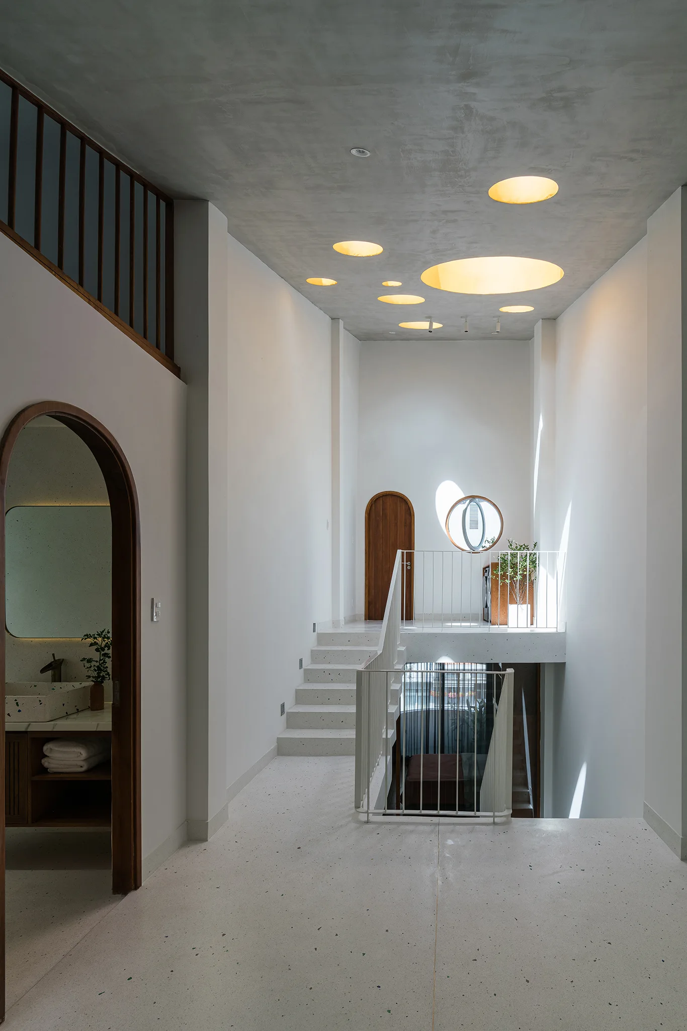 A modern staircase landing with circular ceiling skylights, light-colored terrazzo flooring, white walls, and an arched doorway.