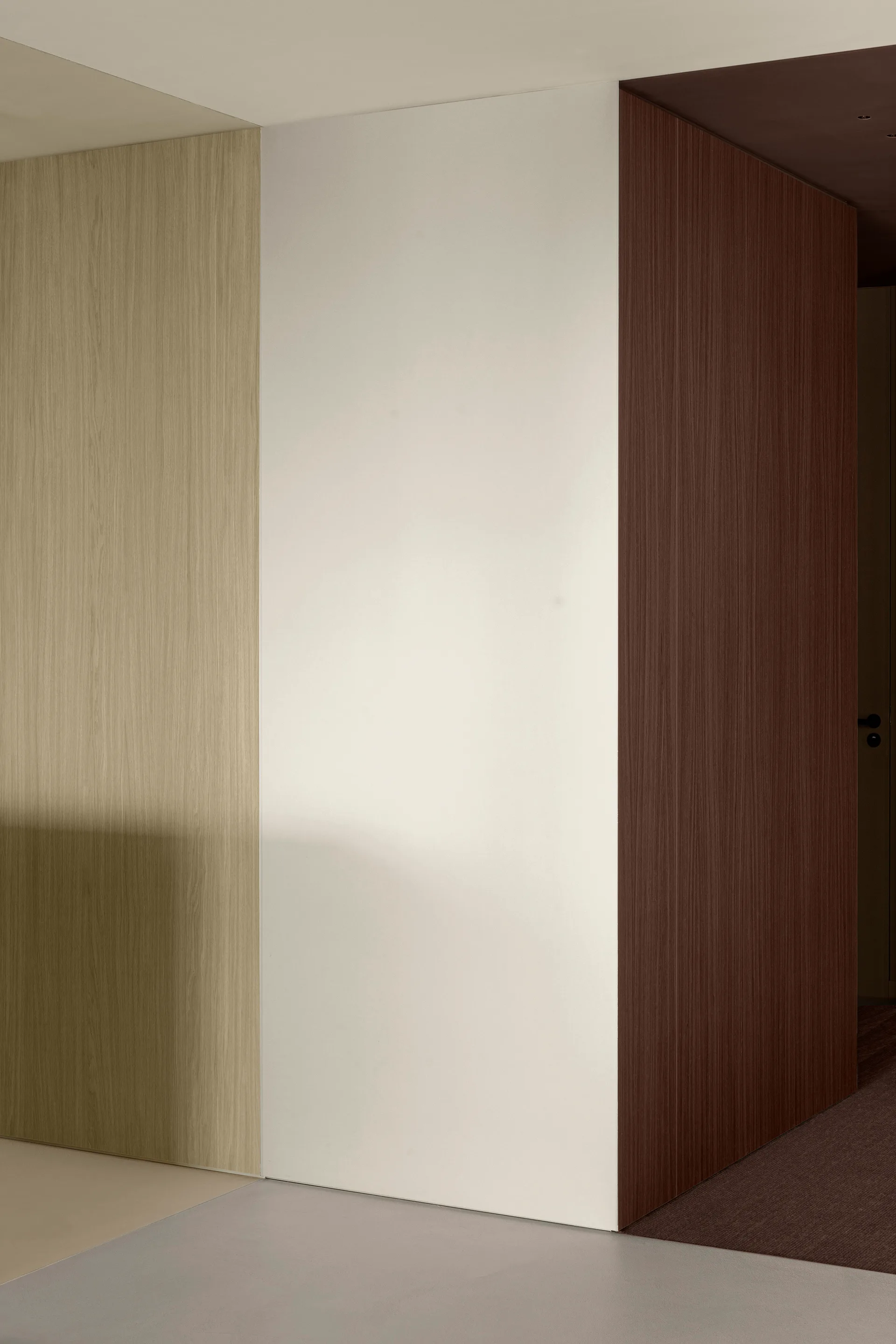 A minimalist interior wall corner composed of light wood veneer, matte white, and dark brown wood panels.