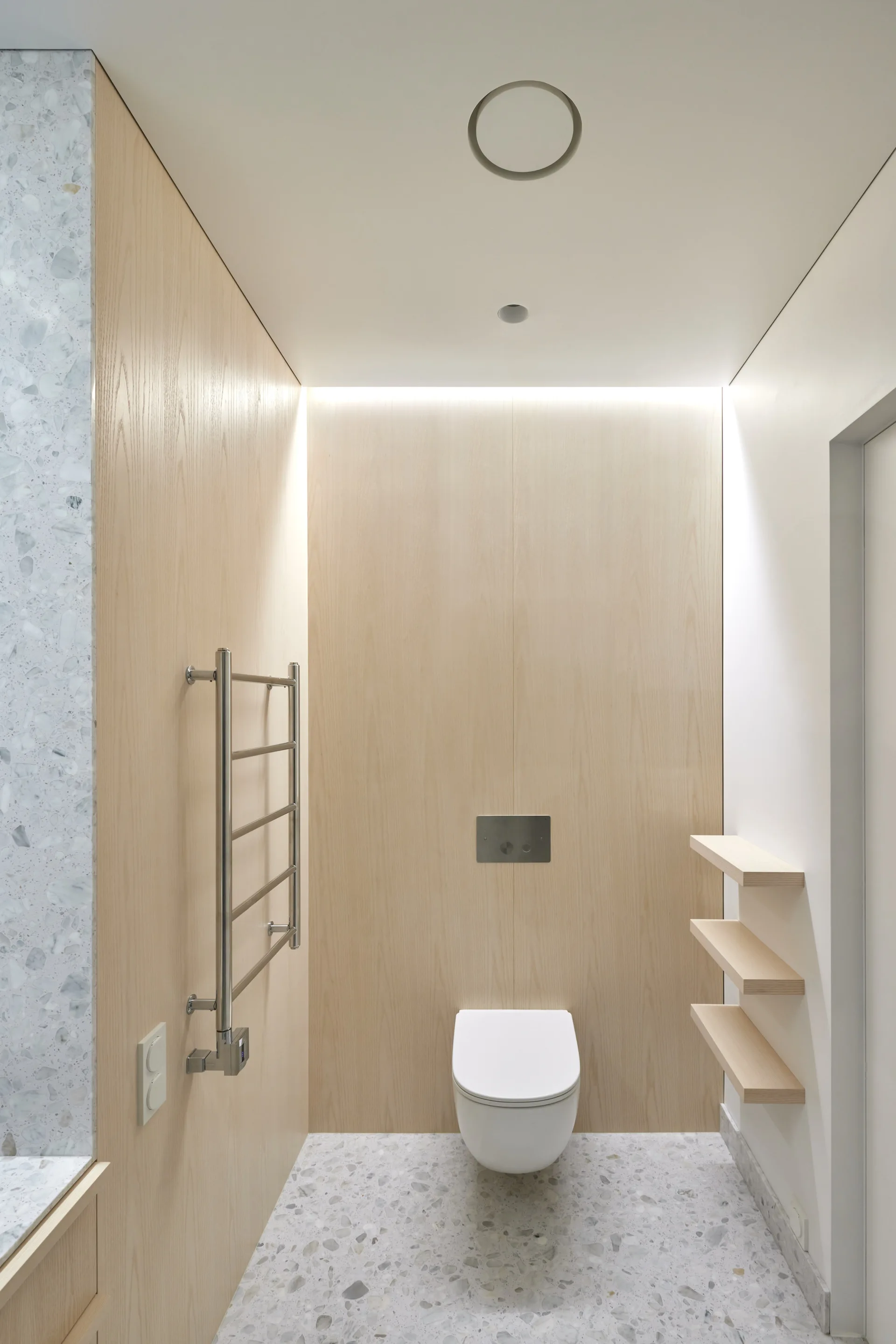 A minimalist powder room with light wood wall paneling, a wall-mounted toilet, and speckled grey and white terrazzo flooring.