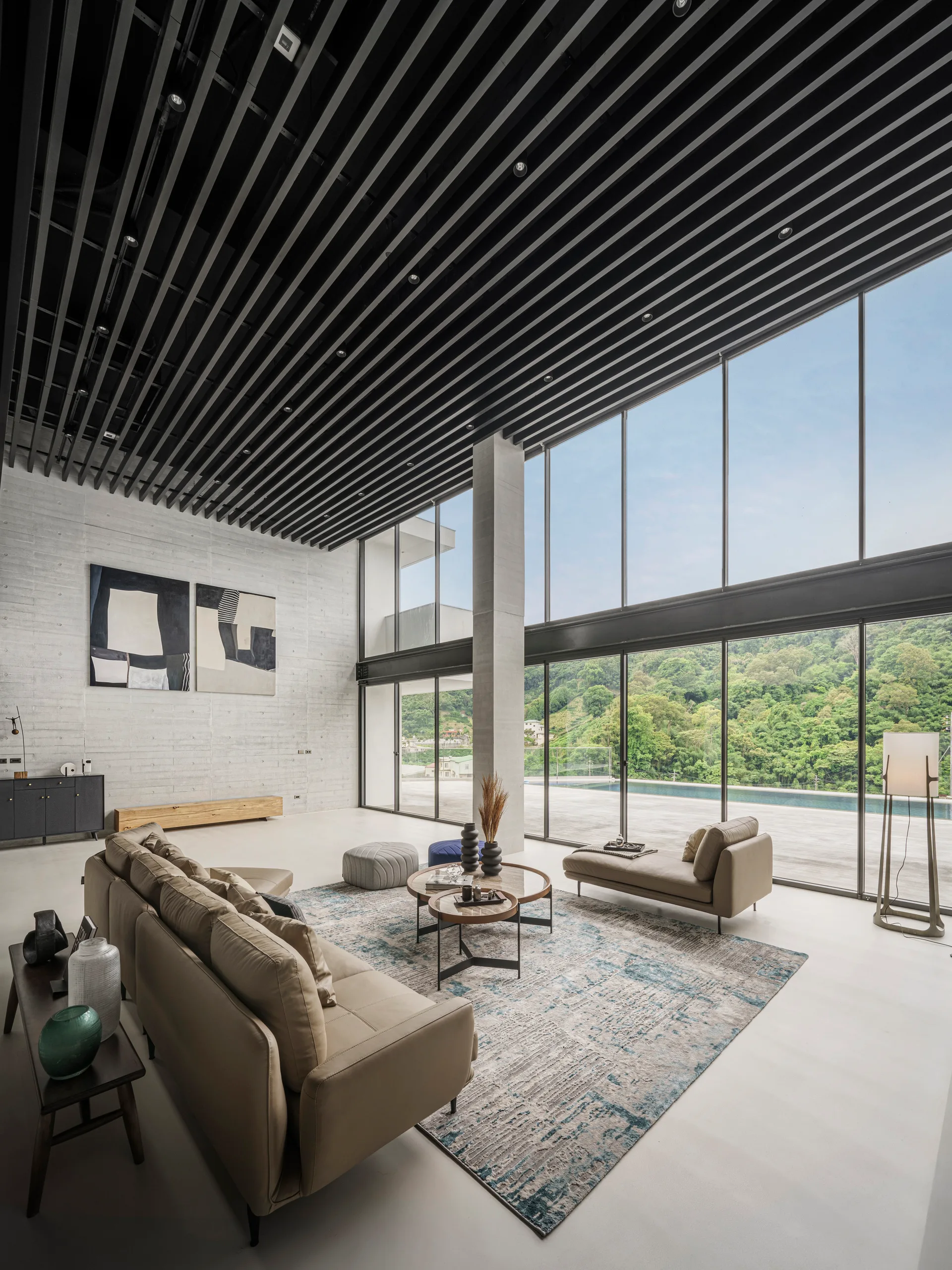 A spacious modern living room featuring a black slat ceiling, textured concrete walls, tan leather seating, and floor-to-ceiling windows.