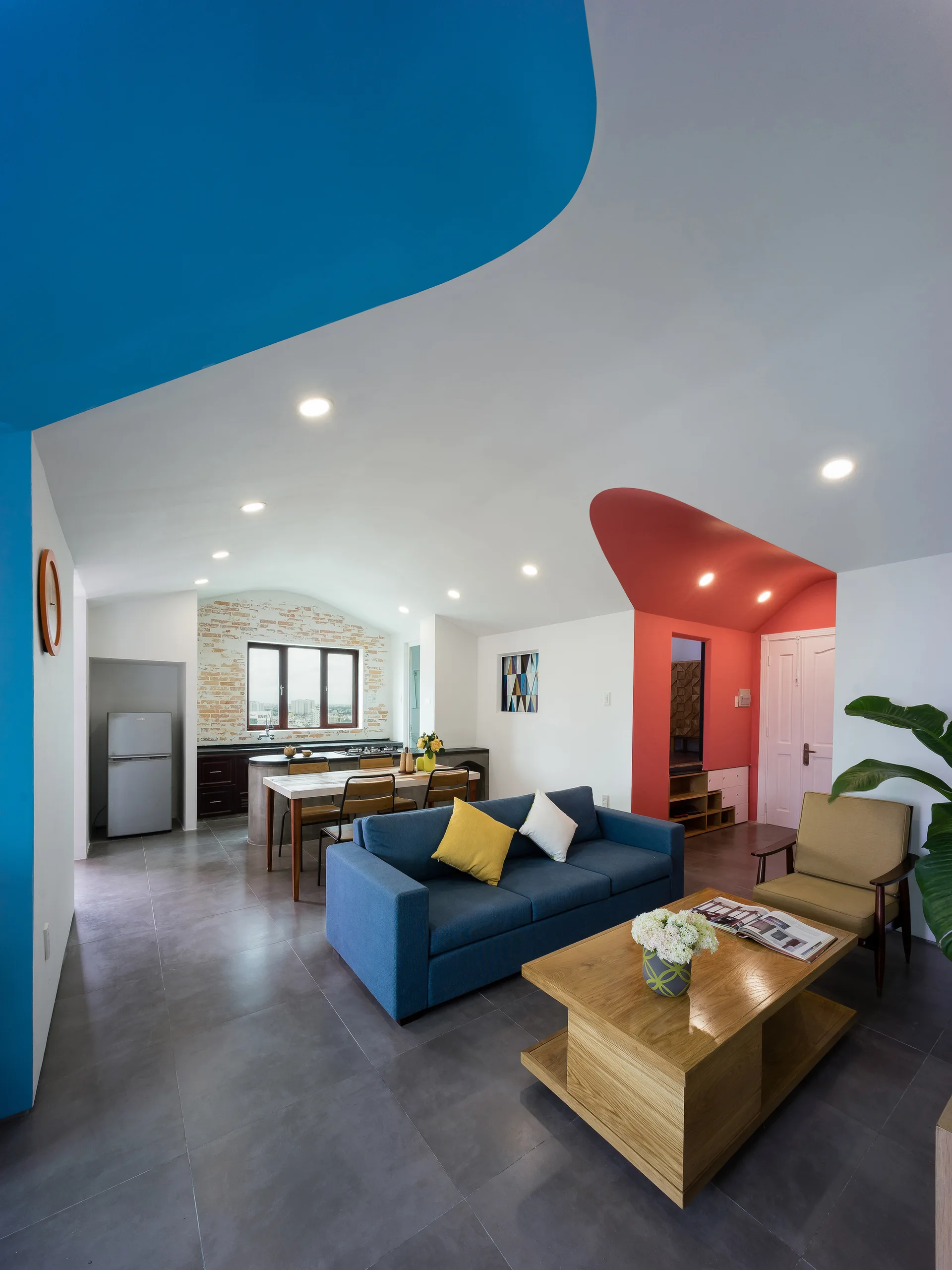 A modern open-concept space with a blue sofa, wooden coffee table, and curved blue and red color-blocked painted sections on the ceiling.