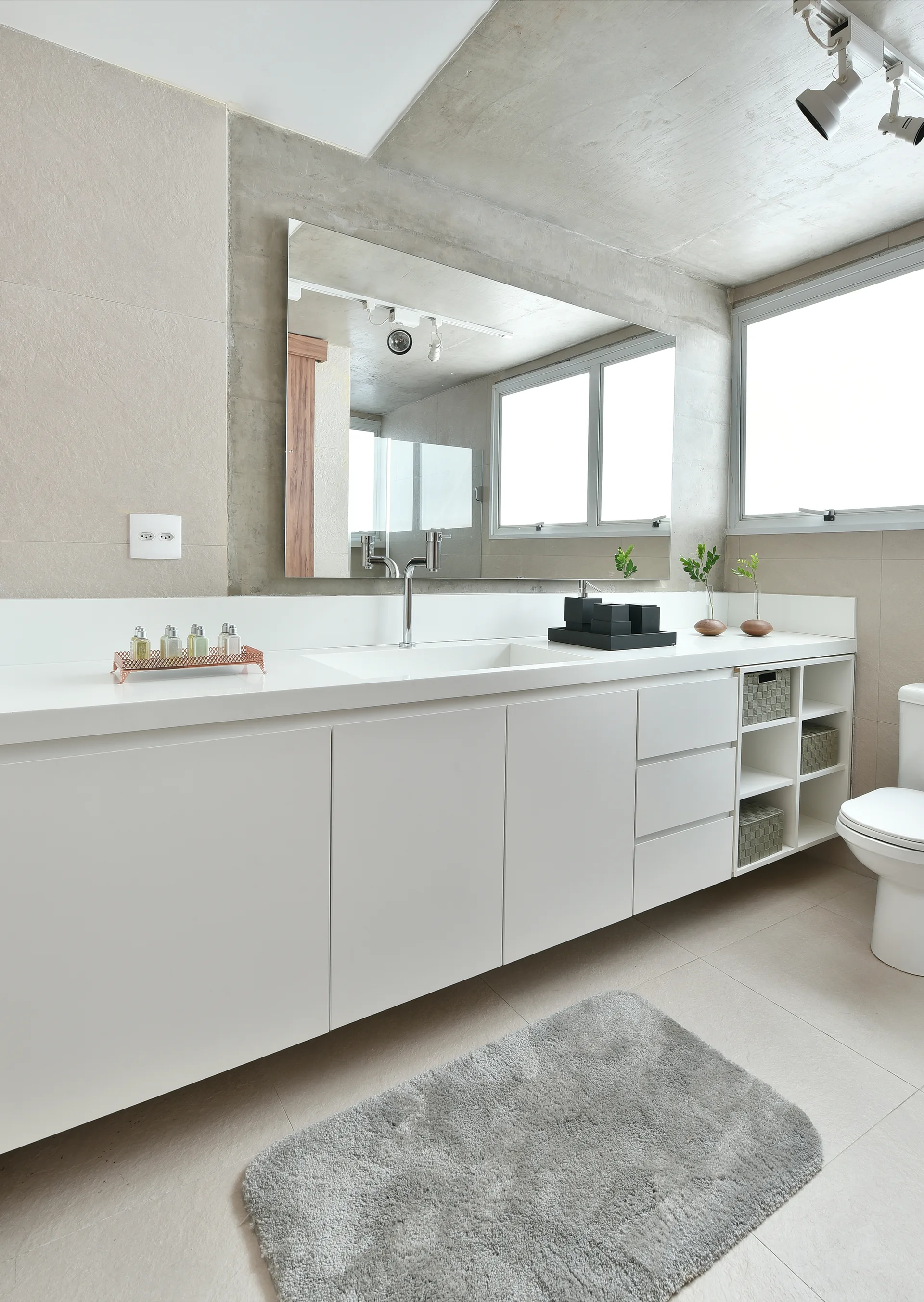A long white vanity with an integrated sink and open storage shelves stands in a bathroom beneath an exposed concrete ceiling.