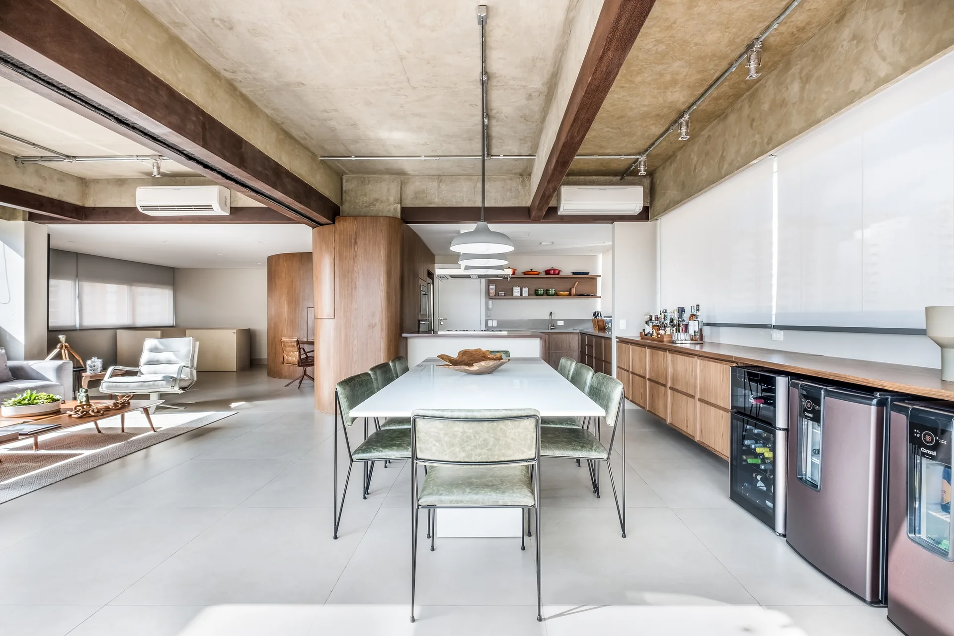 A dining area features a white table with green chairs beneath an exposed concrete ceiling with dark wood beams and a long wooden sideboard.