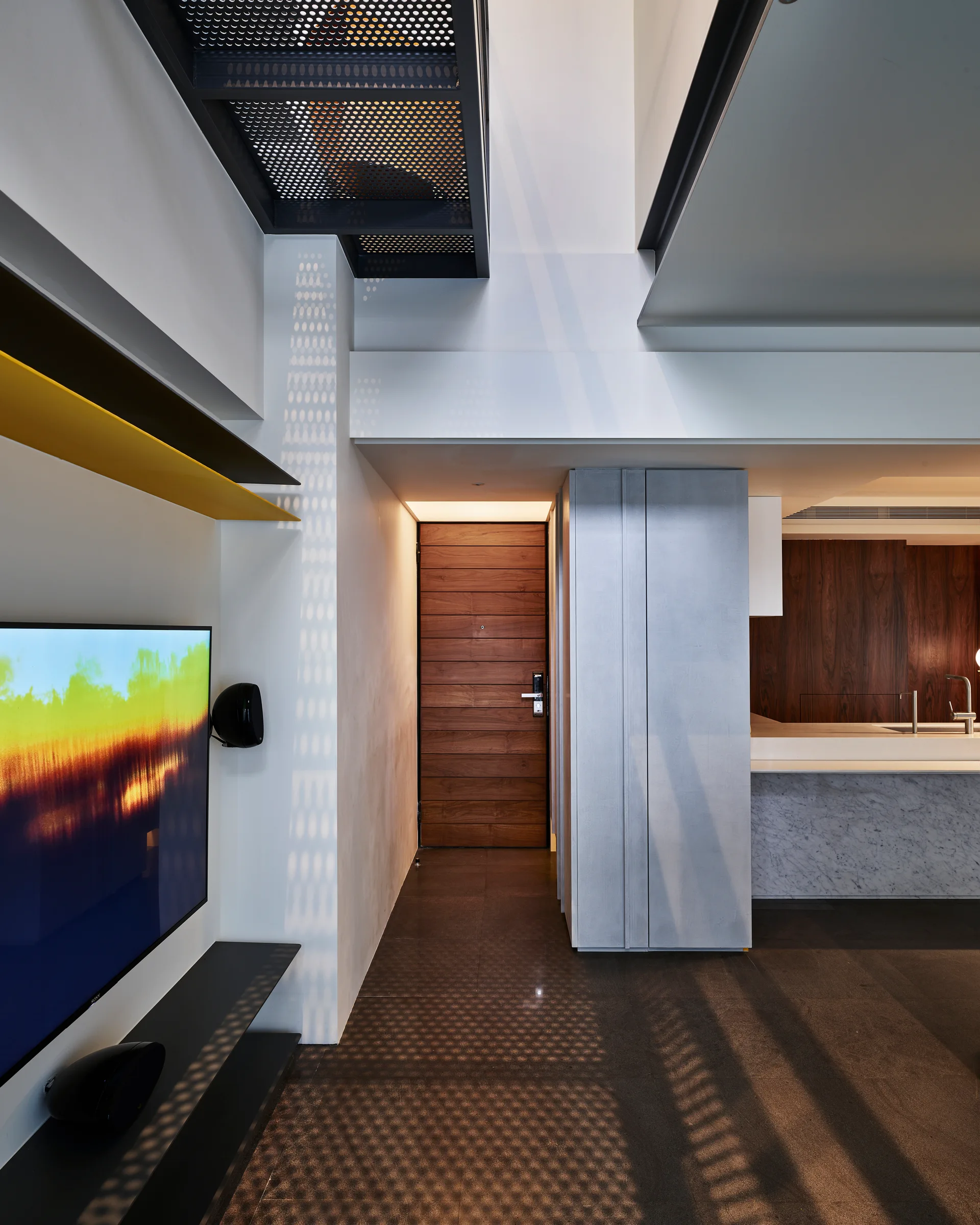 A modern entryway features a dark horizontal-plank wood door, a grey cabinet, and an overhead staircase made of perforated metal.