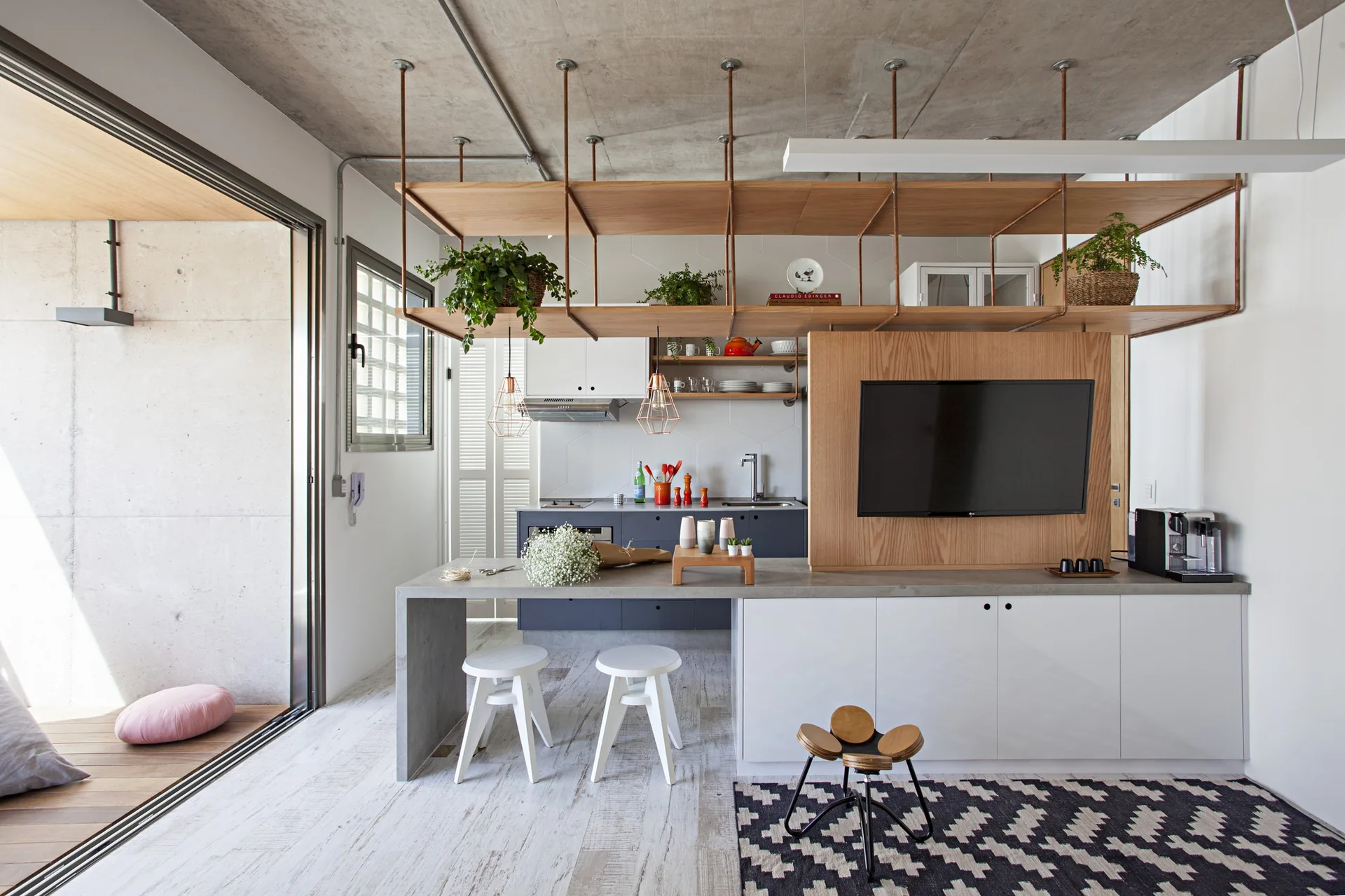 A modern industrial kitchen featuring an exposed concrete ceiling, a concrete-topped kitchen island, and suspended wooden shelving.