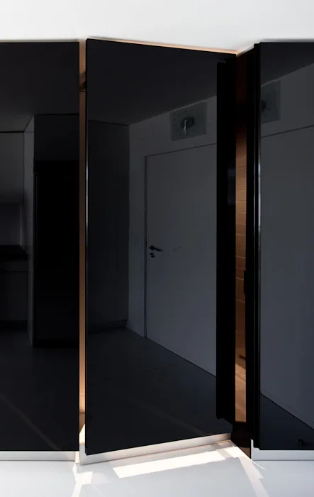 Large high-gloss black cabinet doors with a reflective finish open slightly to reveal warm integrated lighting glowing from the base.
