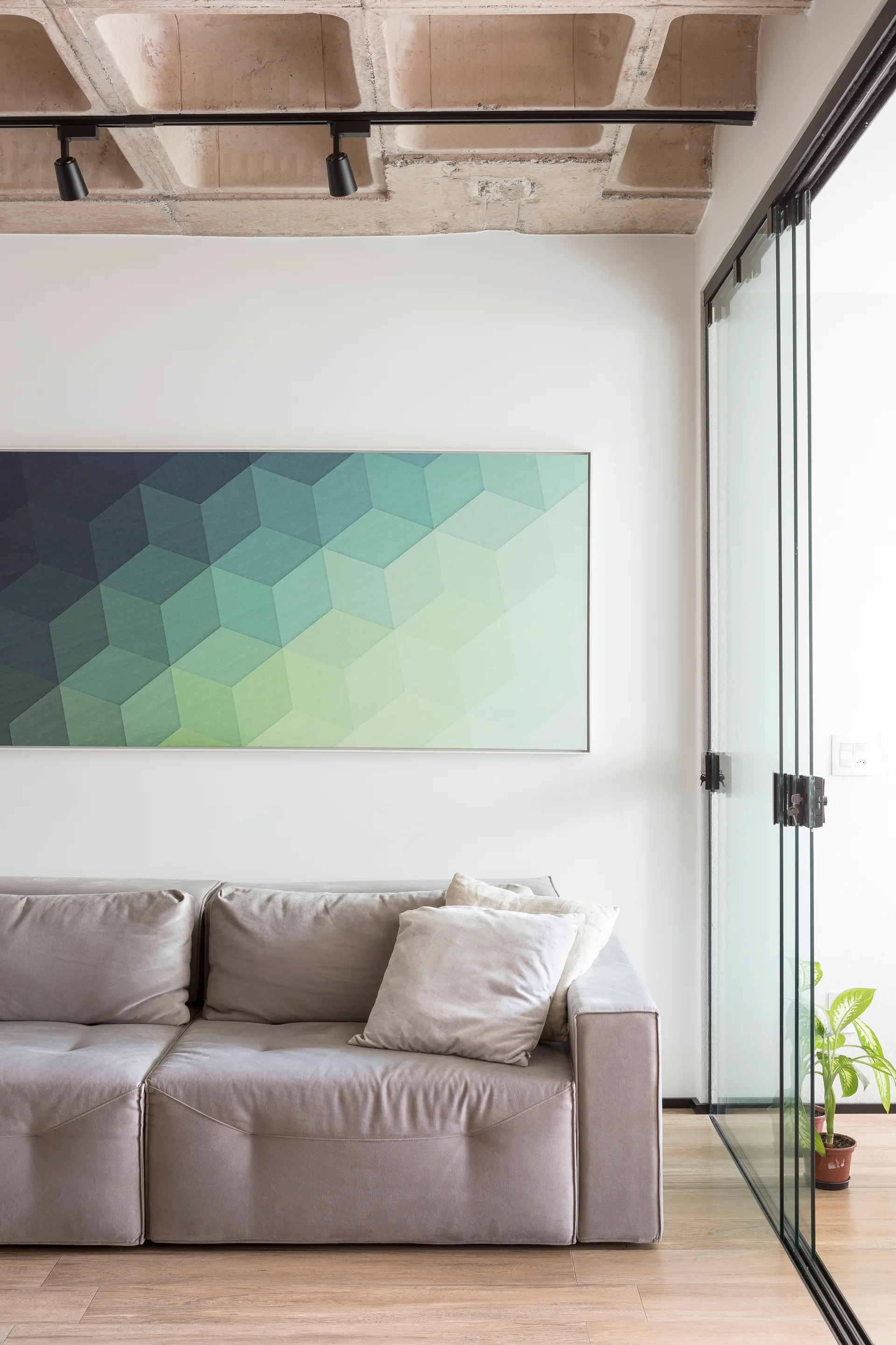 A modern grey sofa sits beneath a geometric green painting in a room with an exposed concrete waffle slab ceiling and sliding glass doors.