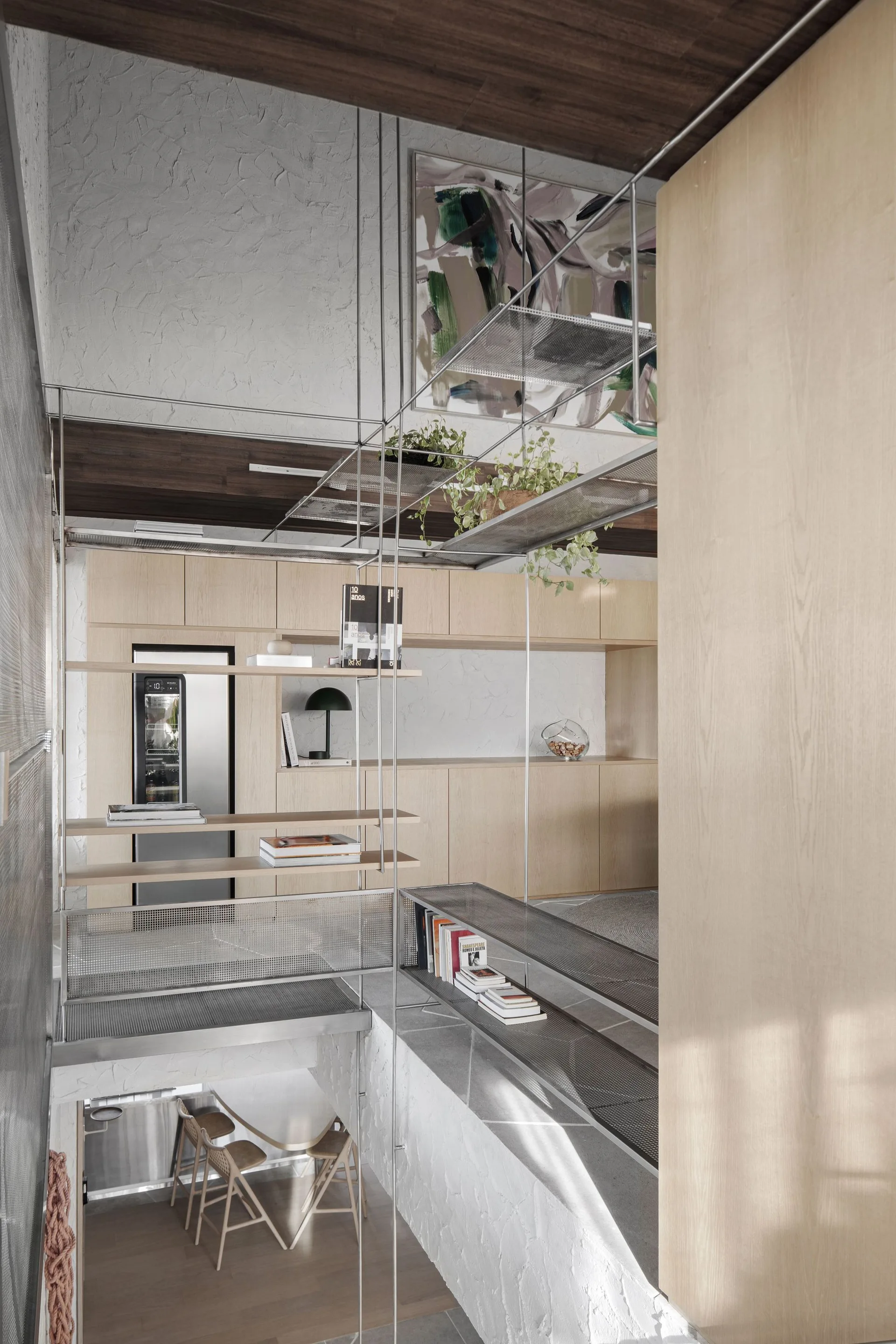 A split-level modern kitchen features light oak built-in cabinets, textured white plaster walls, and an industrial metal mesh shelving system.