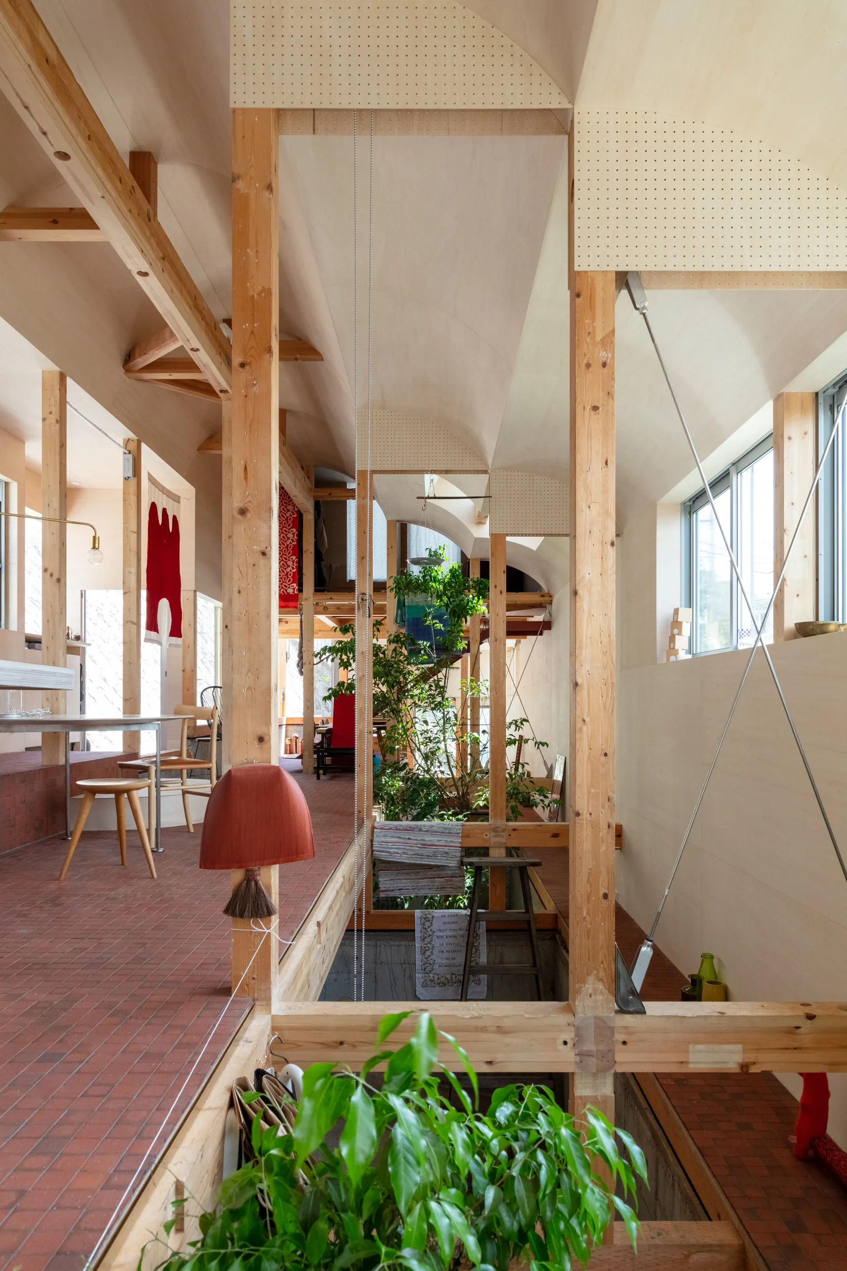 An interior space features exposed light wood timber framing, terracotta tile flooring, an indoor garden, and a curved wooden ceiling.