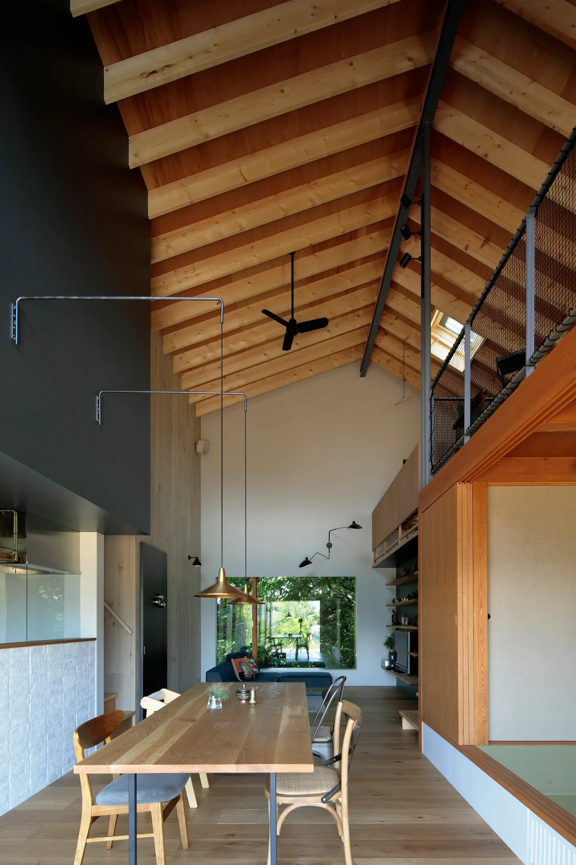 A modern dining room featuring a long wood table under a tall vaulted timber ceiling with exposed rafters and a mezzanine balcony.
