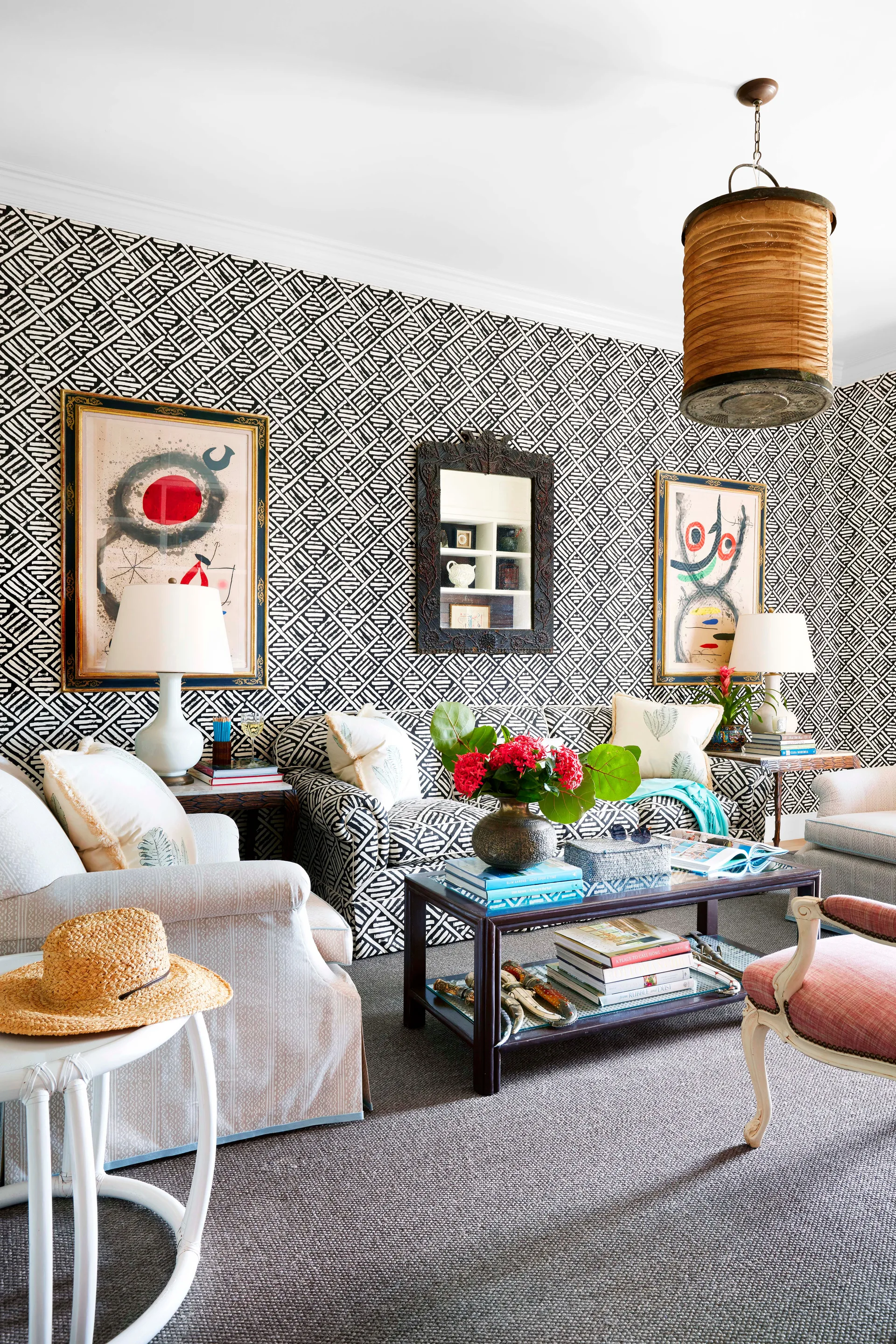 A living room features a sofa and walls covered in matching black and white geometric patterns, flanked by framed artwork and table lamps.