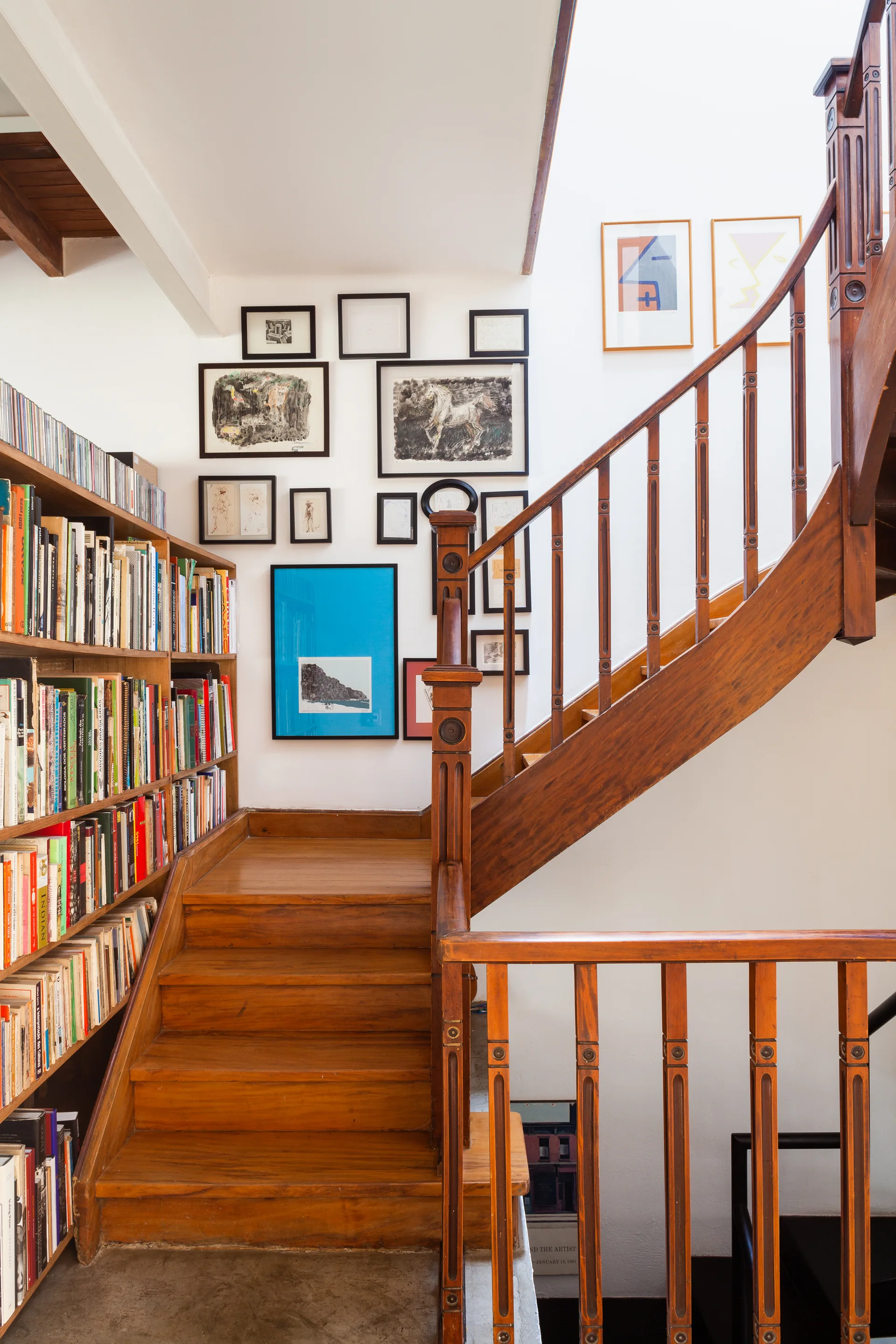 A wooden staircase features built-in bookcases filled with books and a white wall decorated with a gallery of black-framed art.
