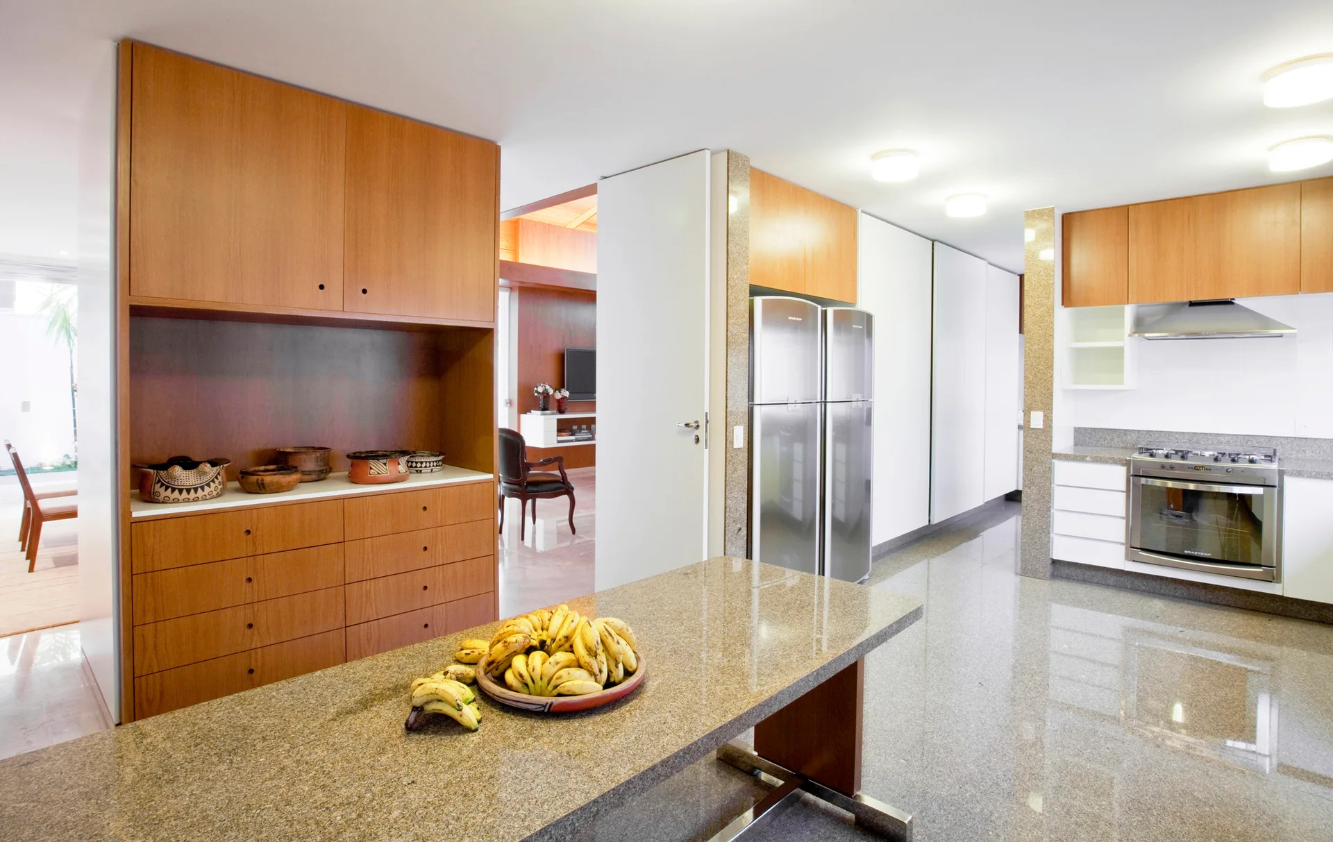 A spacious kitchen featuring warm wood cabinetry, a polished grey stone floor, stainless steel appliances, and a granite island countertop.