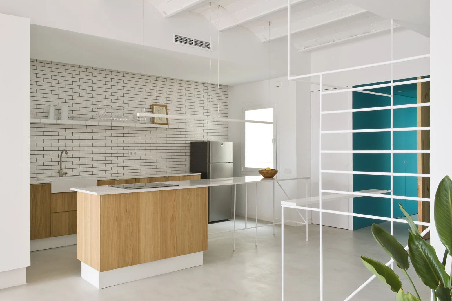 A minimalist kitchen features a wood-front island and lower cabinets, a white subway tile backsplash, and a slender white metal room divider.