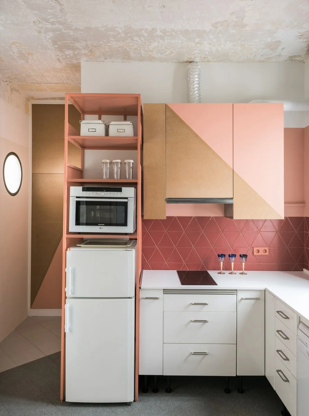 A modern kitchen featuring color-blocked pink and wood upper cabinetry, a red diamond tile backsplash, and a pink metal open shelving unit.