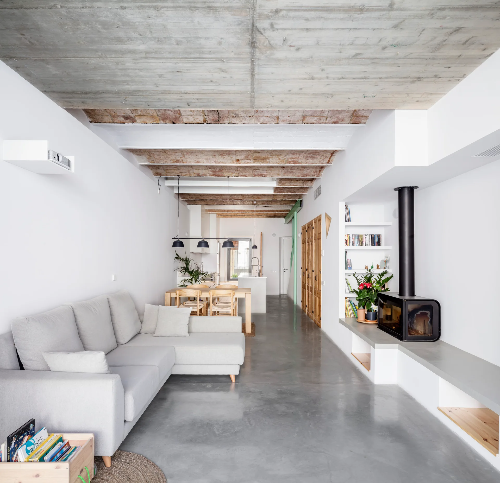 An open-concept living area with a light gray sectional sofa, a modern black fireplace, polished concrete floors, and an exposed concrete ceiling.