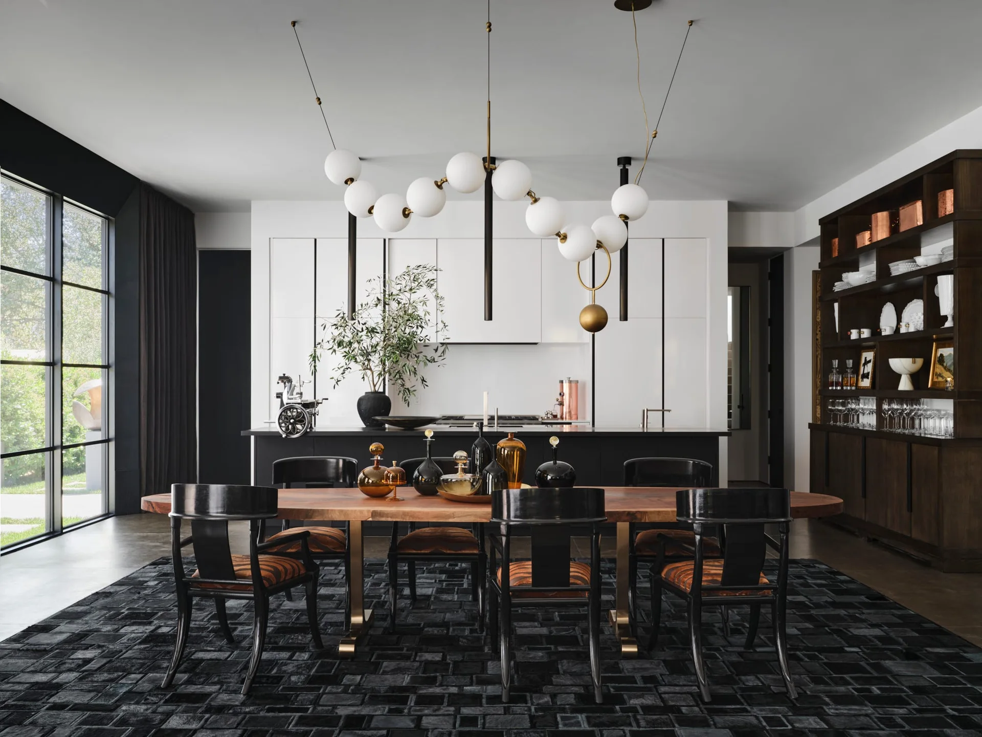 A modern dining room features a natural wood slab table with black chairs on a dark textured rug beneath a sculptural white globe pendant light.