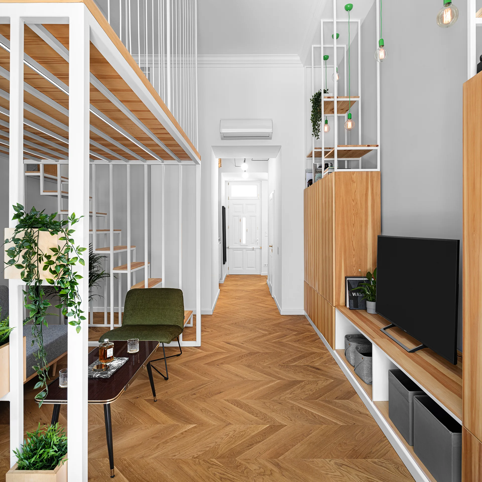 A modern loft apartment featuring a white metal mezzanine structure, custom light oak storage cabinetry, and polished wood herringbone flooring.
