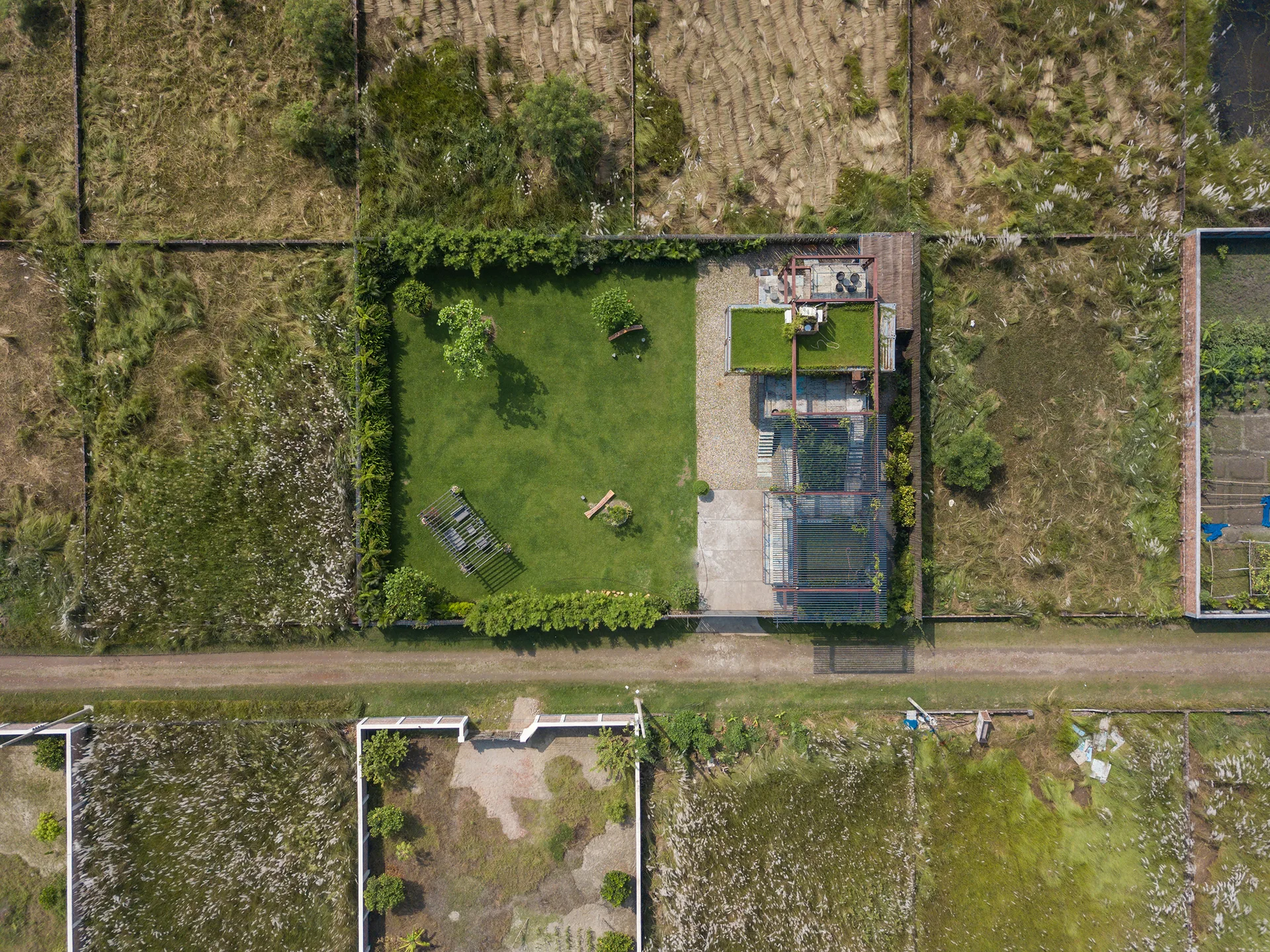 An aerial view of a modern house featuring a green roof next to a large manicured lawn enclosed by perimeter hedges and pergolas.