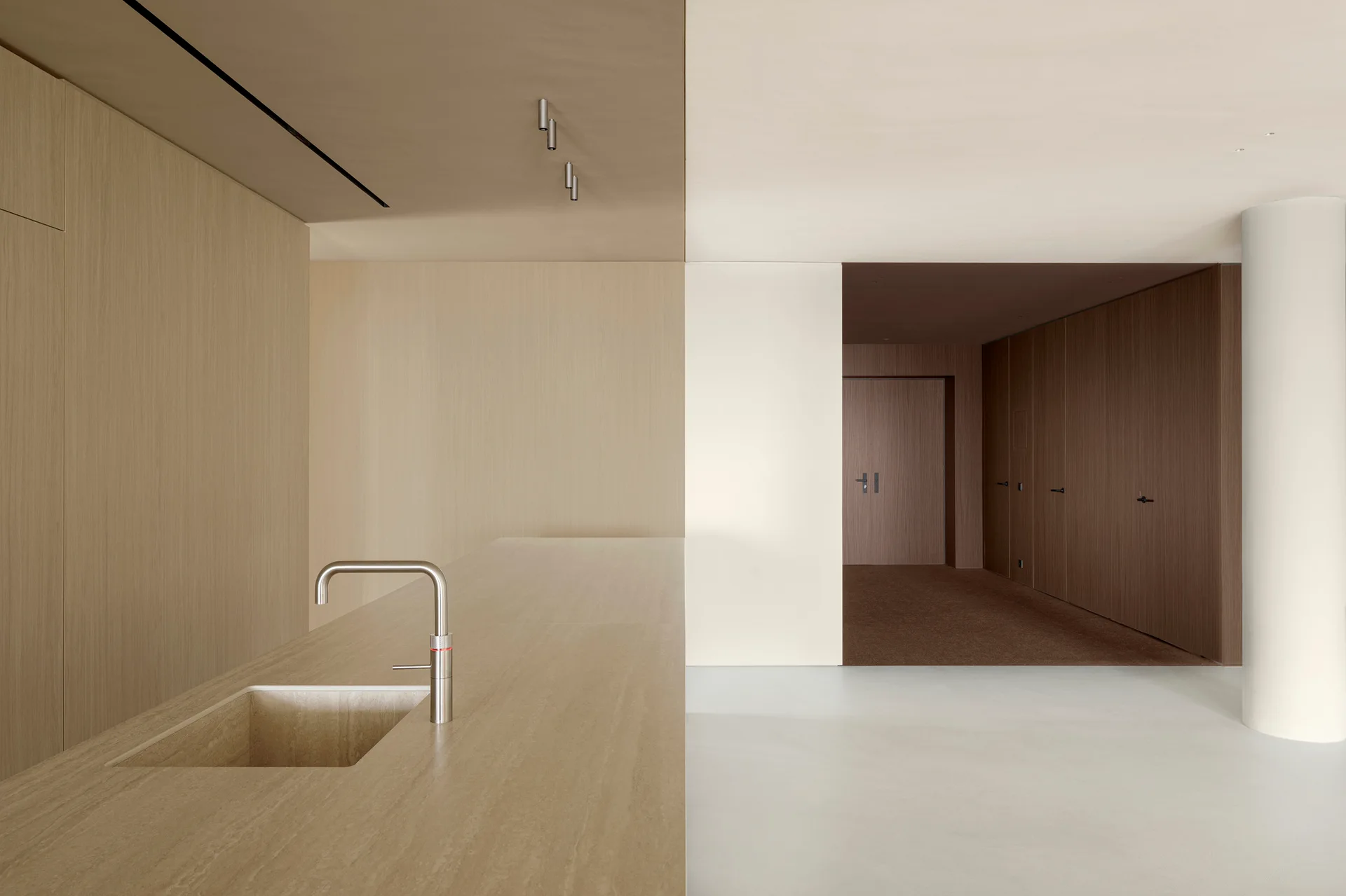 A minimalist kitchen featuring a beige stone island with an integrated sink and metal faucet, set against seamless wood-paneled walls.
