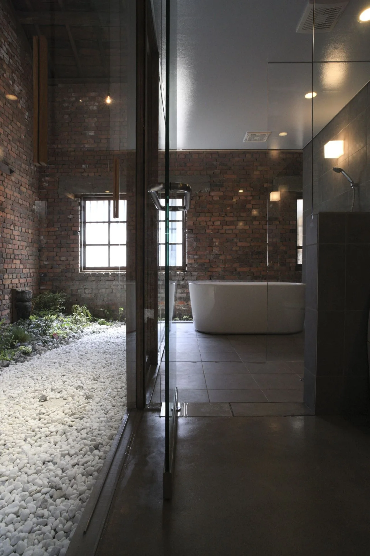 A modern bathroom featuring an oval freestanding bathtub next to a glass partition that reveals an indoor rock garden with white pebbles.