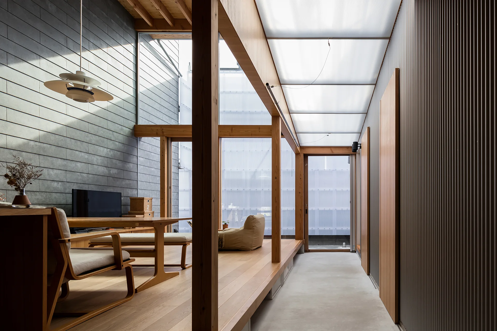 A modern Japanese-style living space features a raised wooden platform, exposed timber posts, concrete block walls, and a translucent paneled ceiling.
