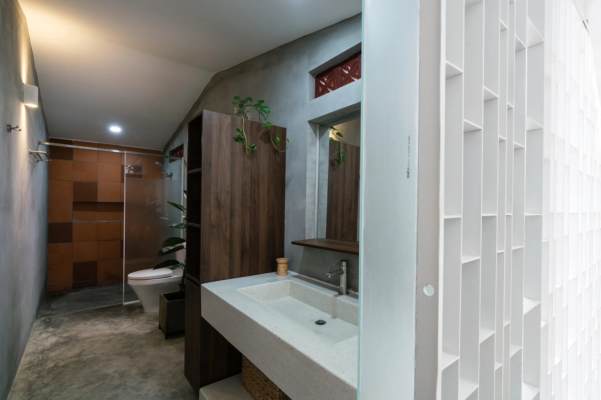 A modern bathroom features a concrete sink vanity next to a tall wood cabinet, with a white geometric screen and concrete walls.