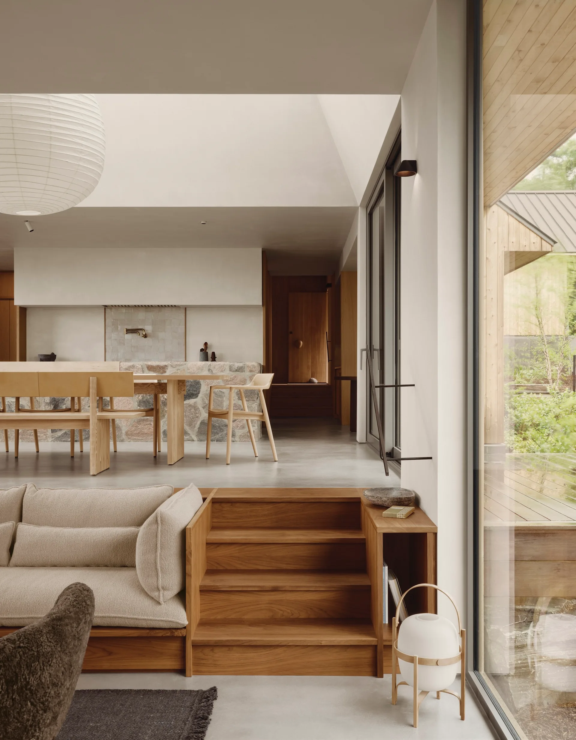 A split-level interior featuring wooden steps leading from a sunken living room with a cream sofa to a dining space with a stone-clad kitchen island.