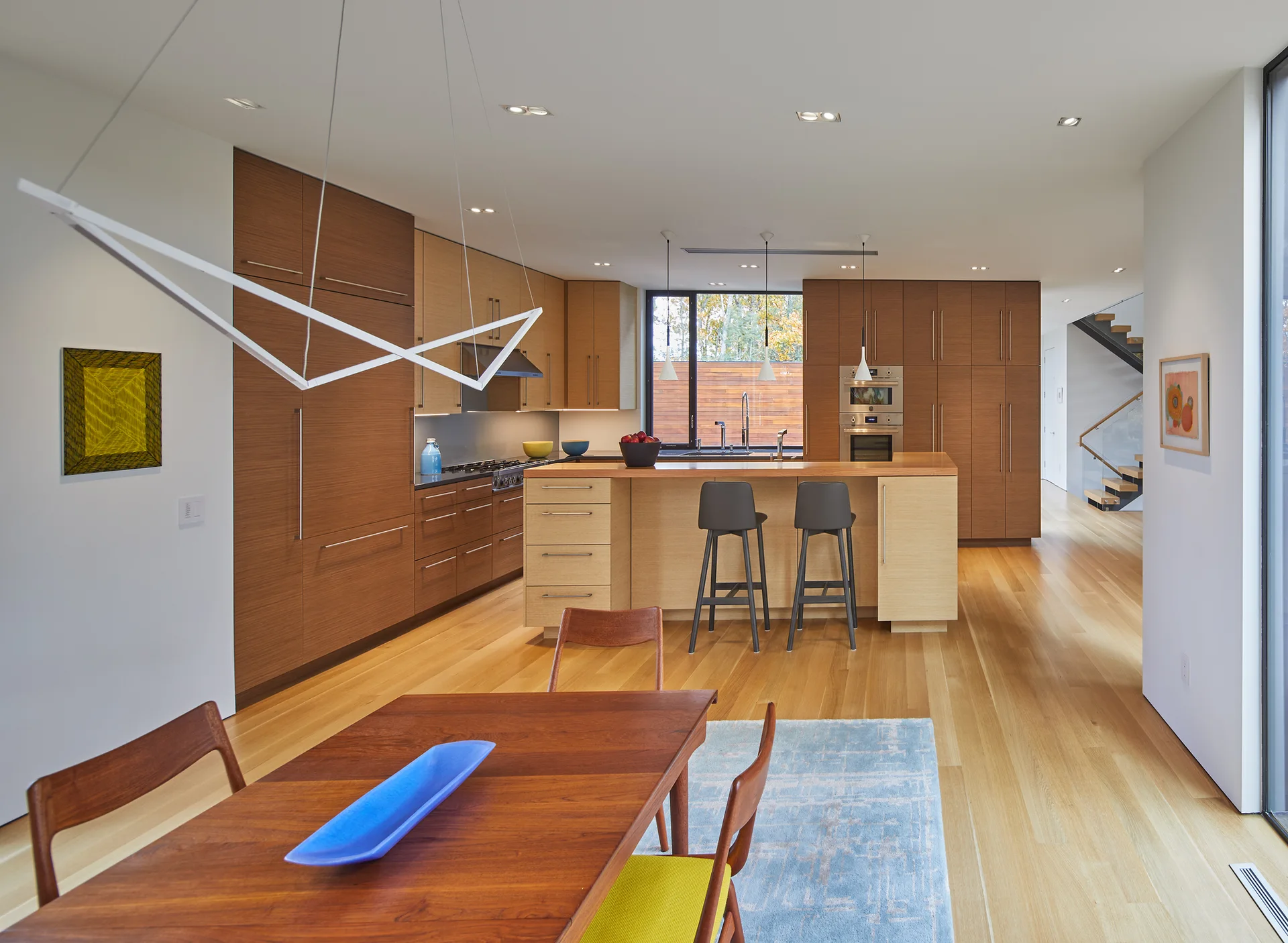 A spacious kitchen and dining area featuring warm wood cabinetry, a central island with barstools, and a wooden dining table over a light blue rug.