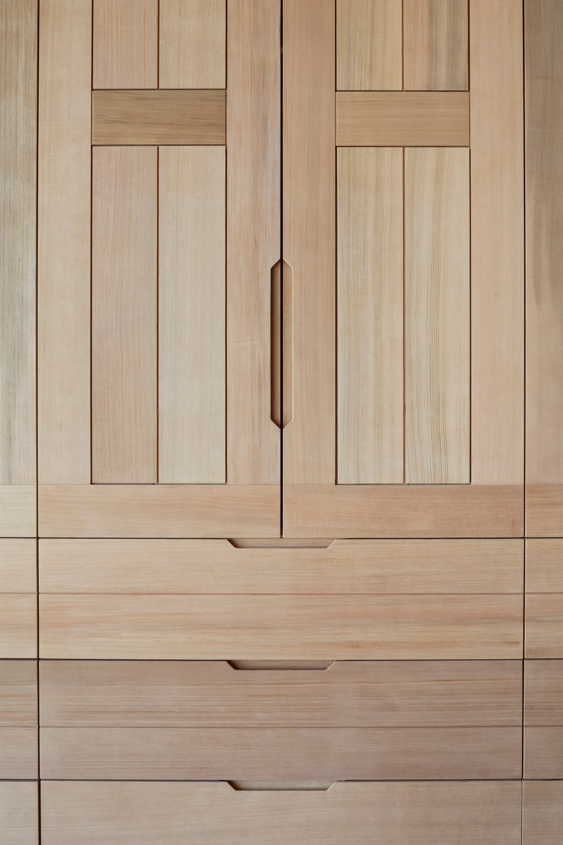 Close-up of natural light wood cabinet doors and drawers featuring vertical wood grain panels and carved integrated handle pulls.