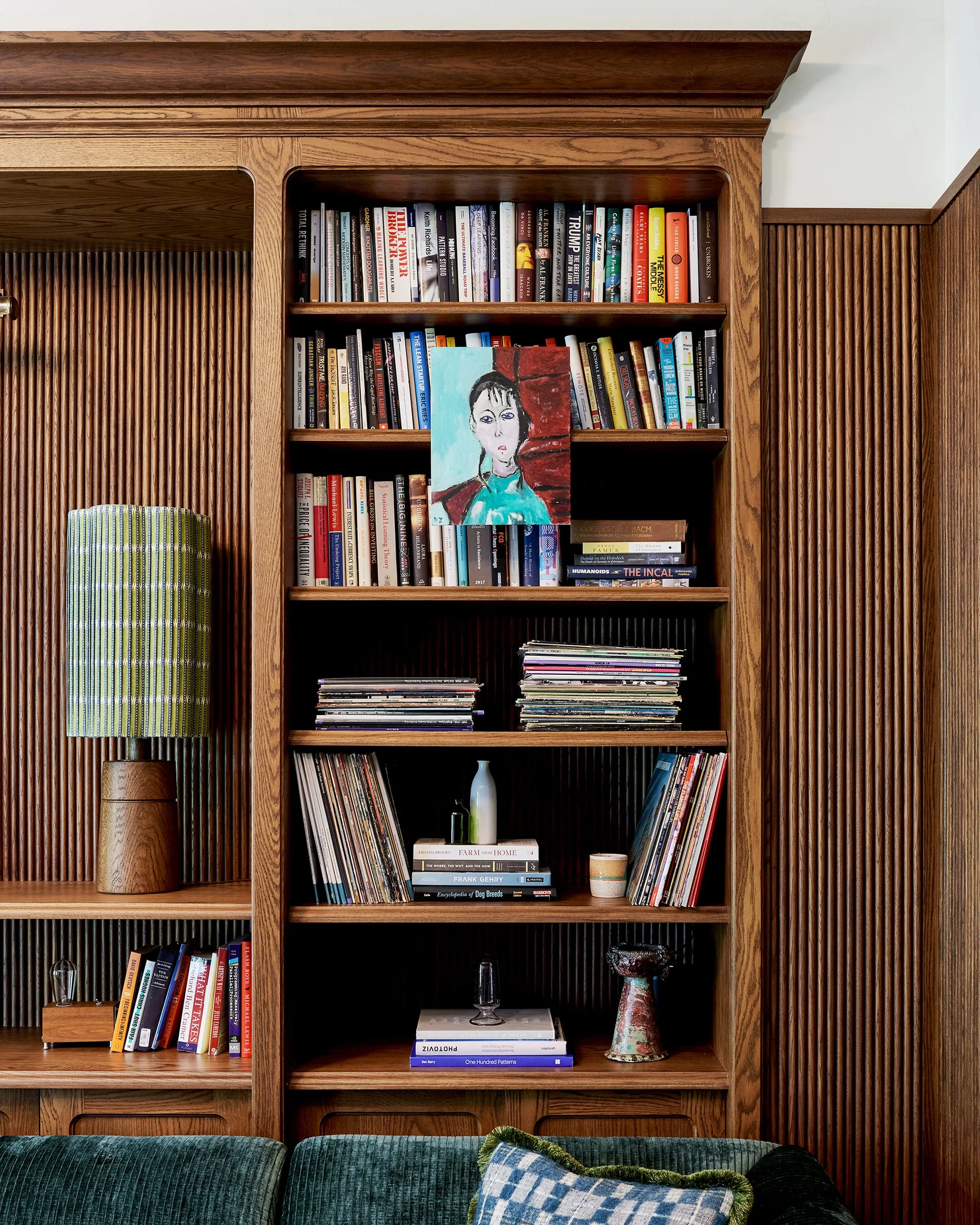 Built-in wooden bookshelves filled with books and a table lamp are set against a vertical slatted wood paneled wall.